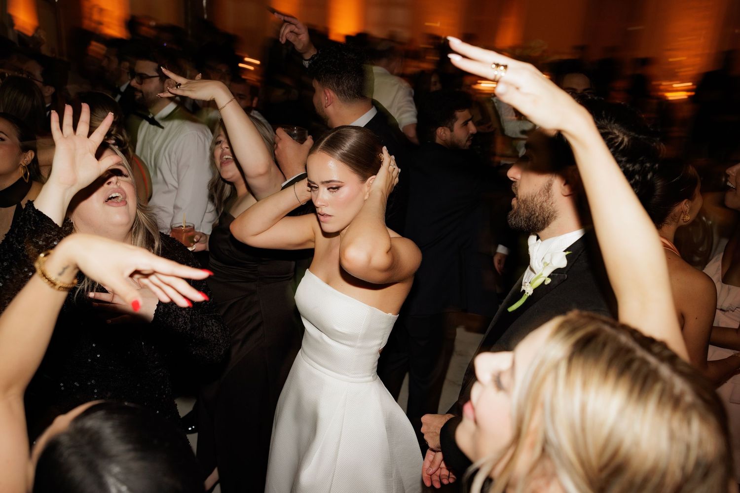 People dancing energetically at a wedding reception with raised hands as the bride in white dress moves on the dance floor.