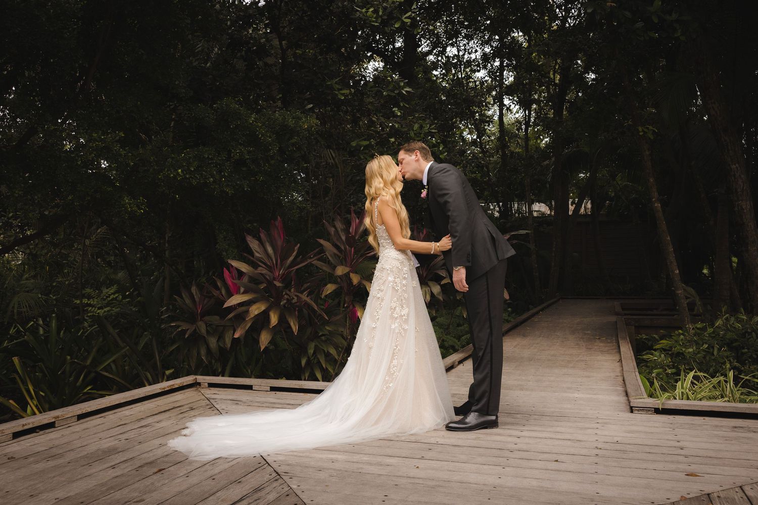 An intimate wedding moment captured on an outdoor stone path surrounded by greenery and garden architecture.