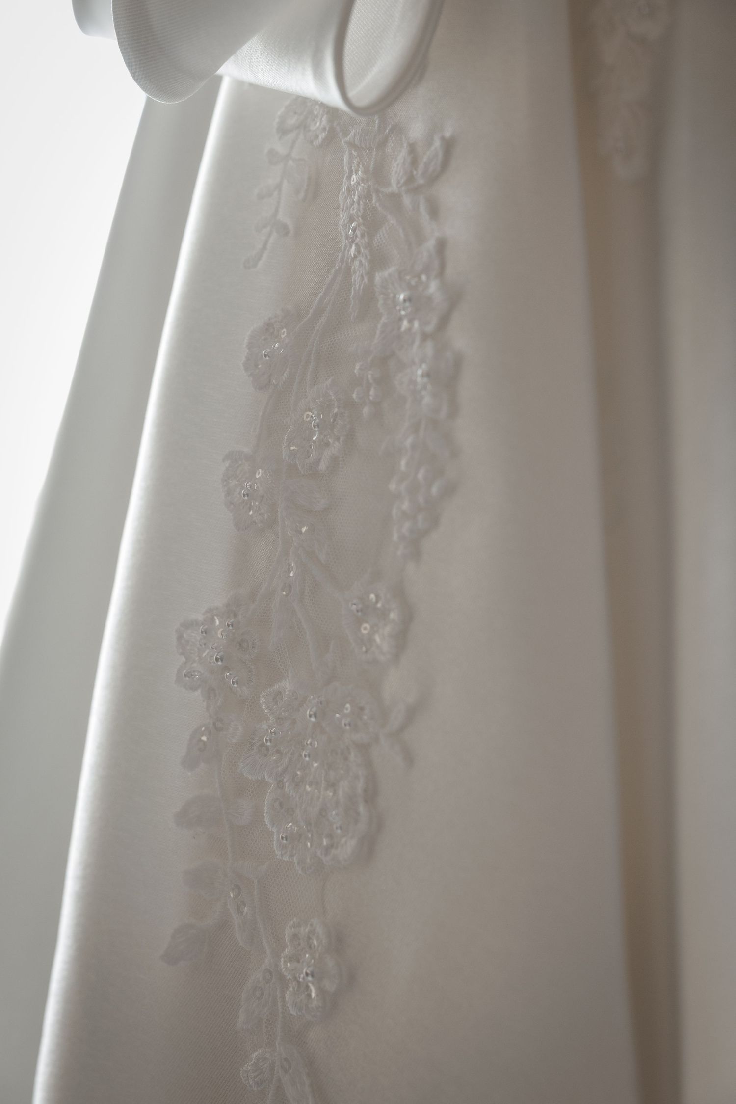 Close-up detail of delicate white lace embroidery on a wedding dress fabric.