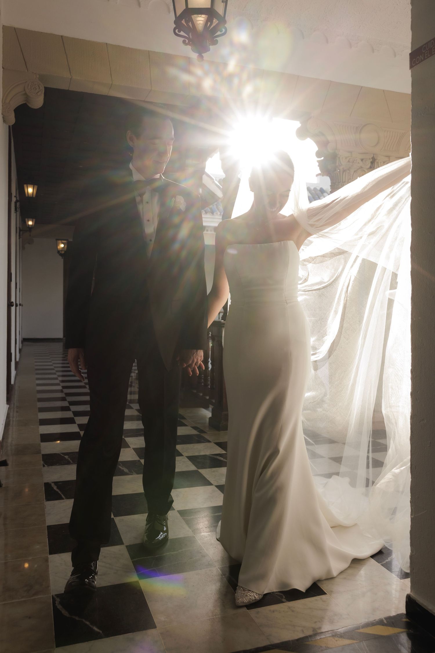 A dance floor with a black and white checkered pattern glows dimly beneath wedding attire silhouettes.