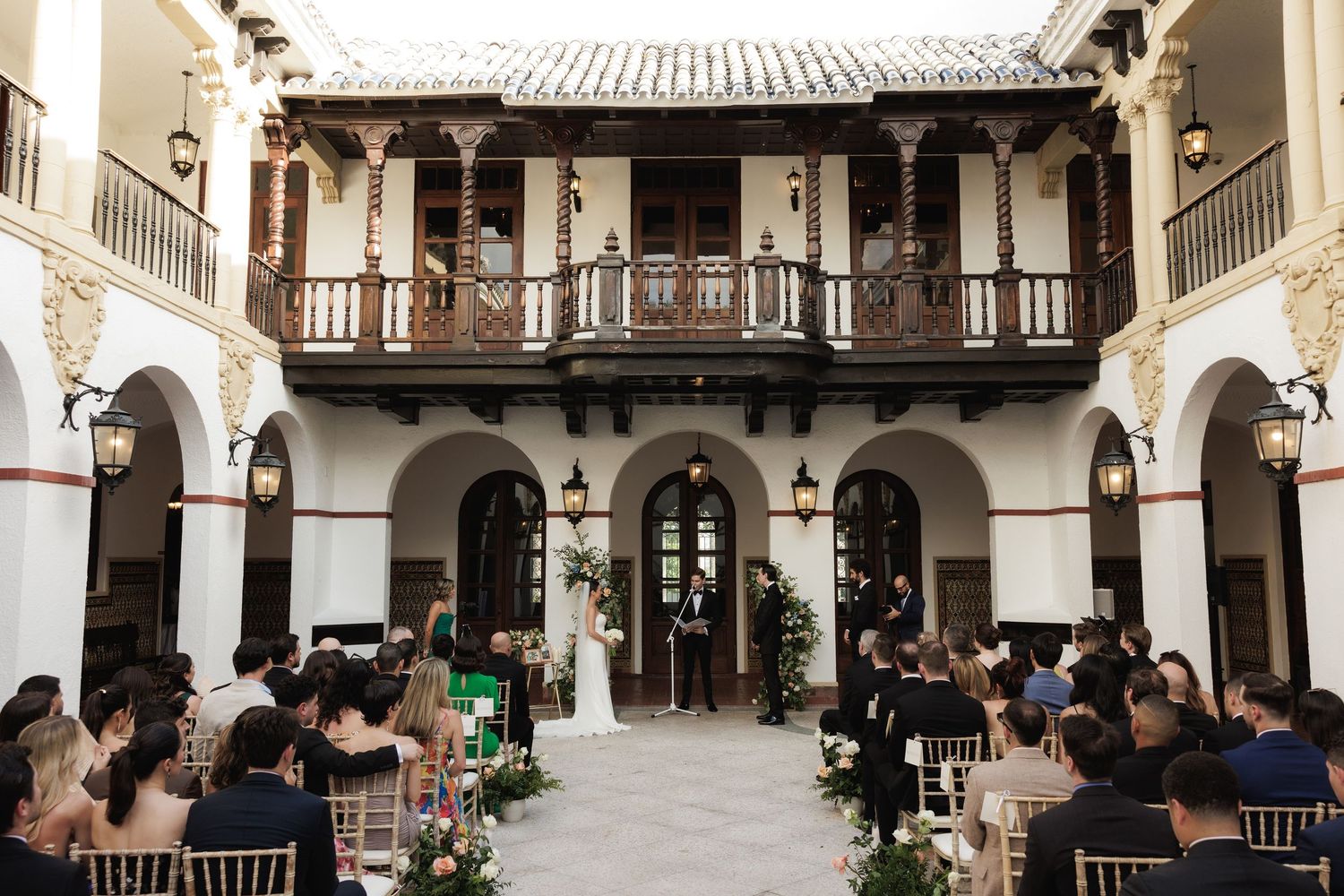 Wedding ceremony setup in a Spanish colonial courtyard with arched walkways and wooden balconies.
