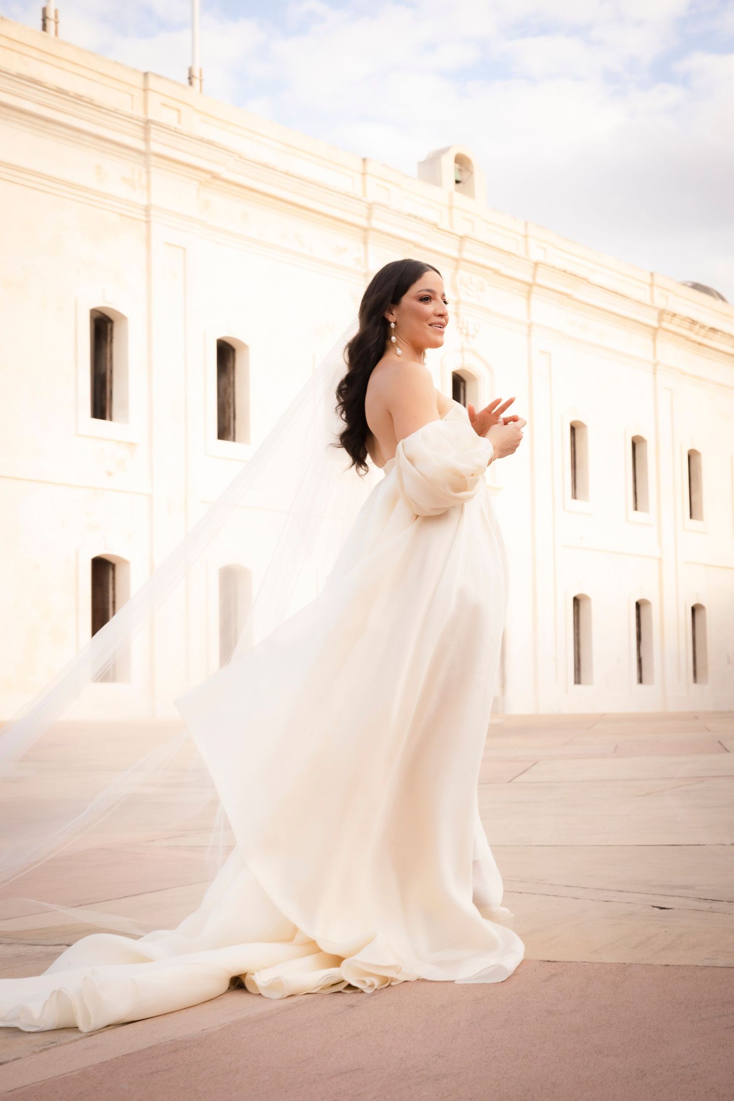A flowing white wedding gown twirls against a bright white colonial building exterior.
