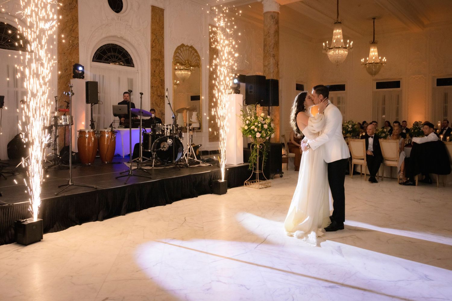 Wedding reception ballroom with dramatic lighting effects, stage setup, and elegant white decor.