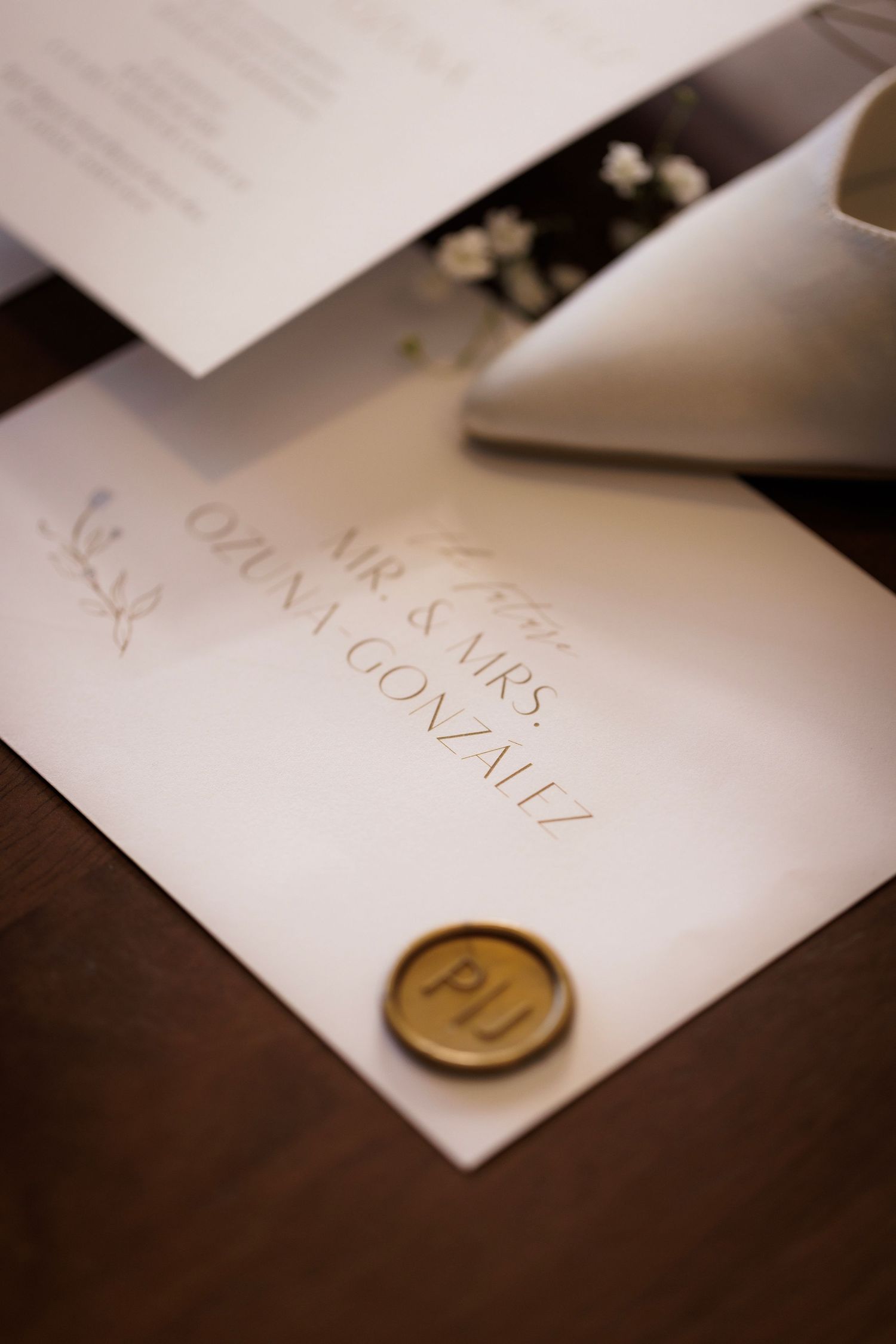 Elegant wedding invitation with handwritten calligraphy text and golden wax seal on white paper.