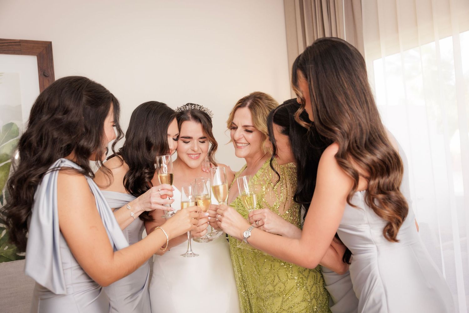 Bridesmaids in elegant dresses toast with champagne glasses during a wedding celebration indoors.
