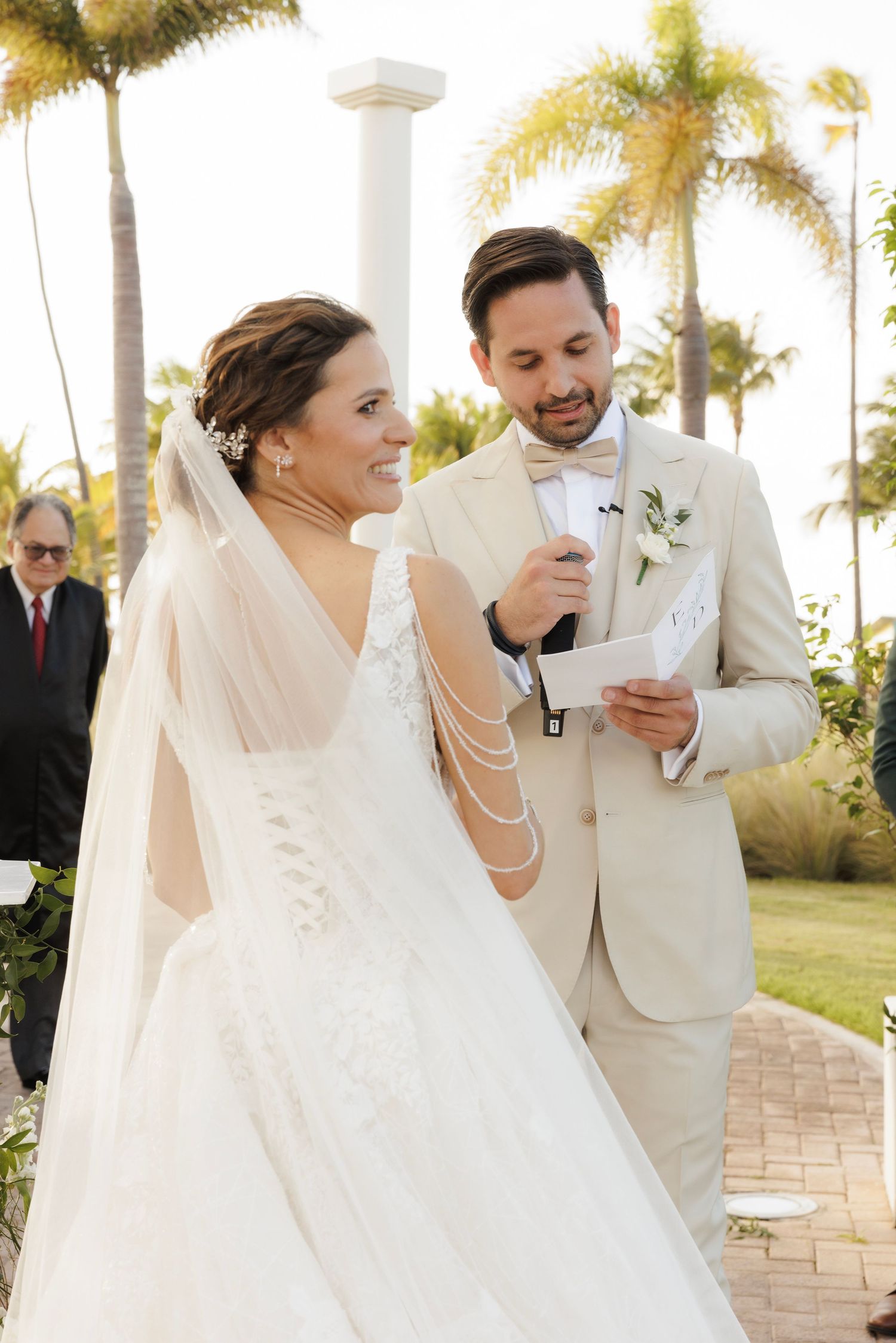 A wedding couple shares a joyful moment during their ceremony in a palm tree-lined outdoor venue.