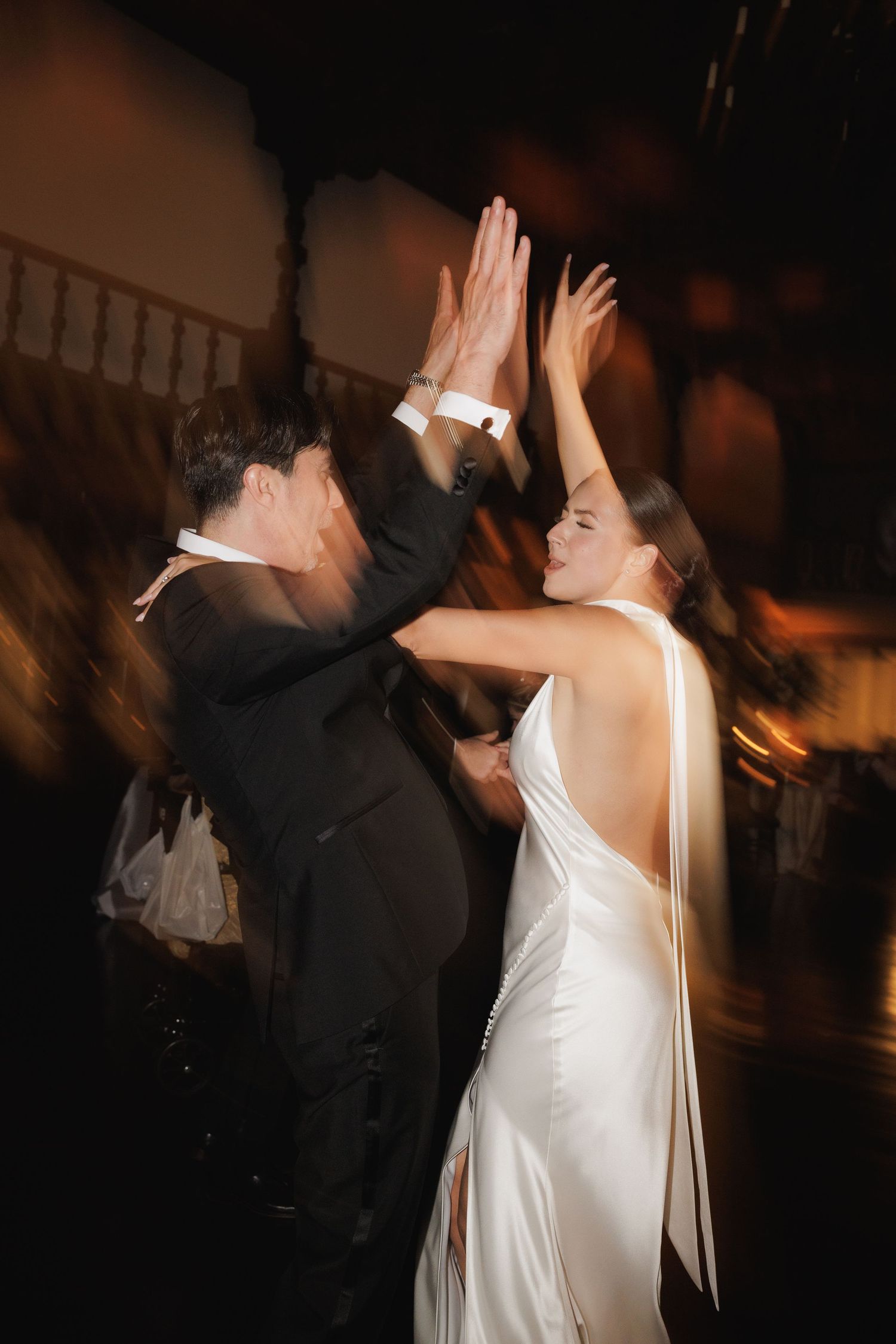 Wedding couple dances energetically in a dark reception venue with motion blur effects.