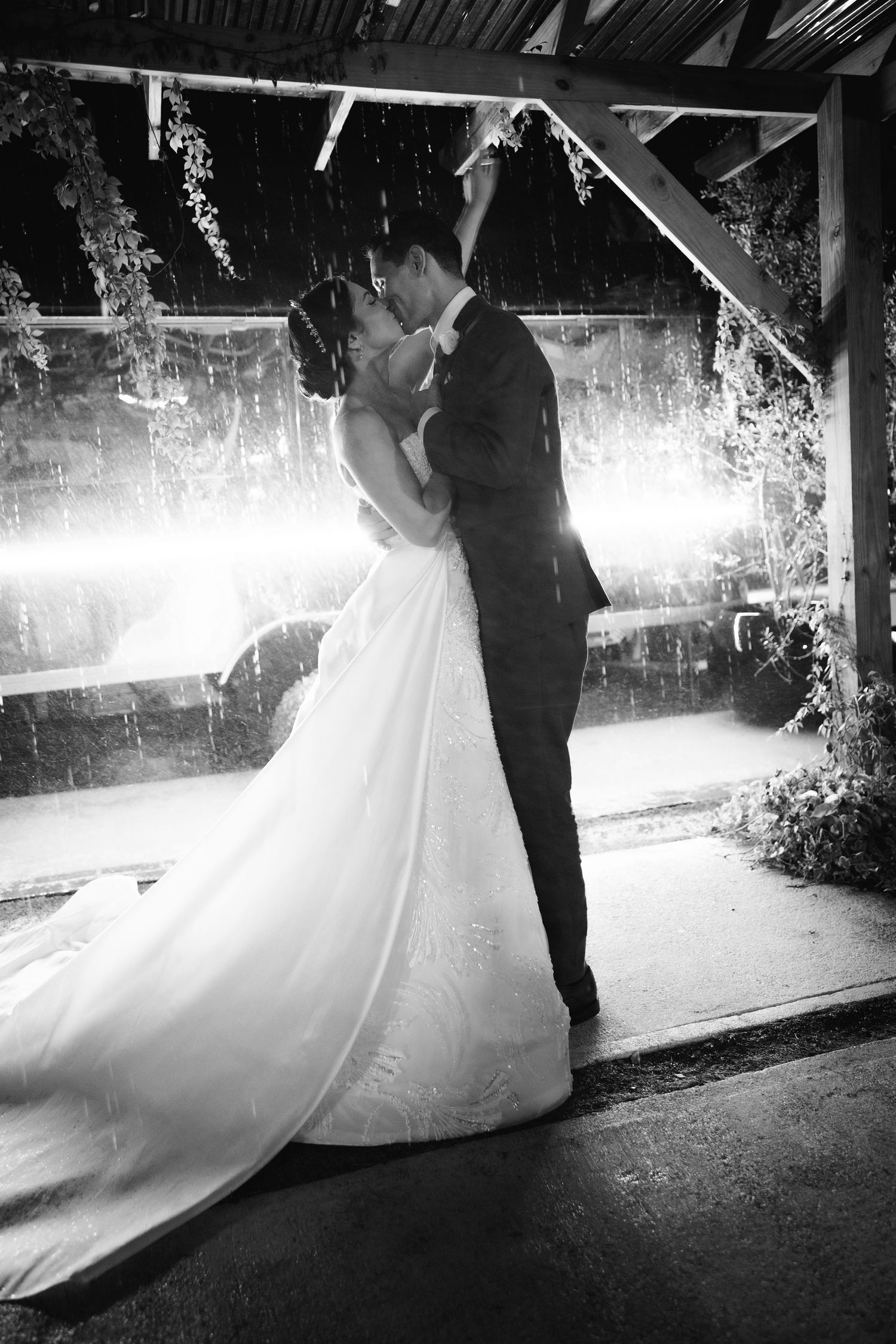 A romantic couple dancing in dramatic black and white lighting under a covered walkway.