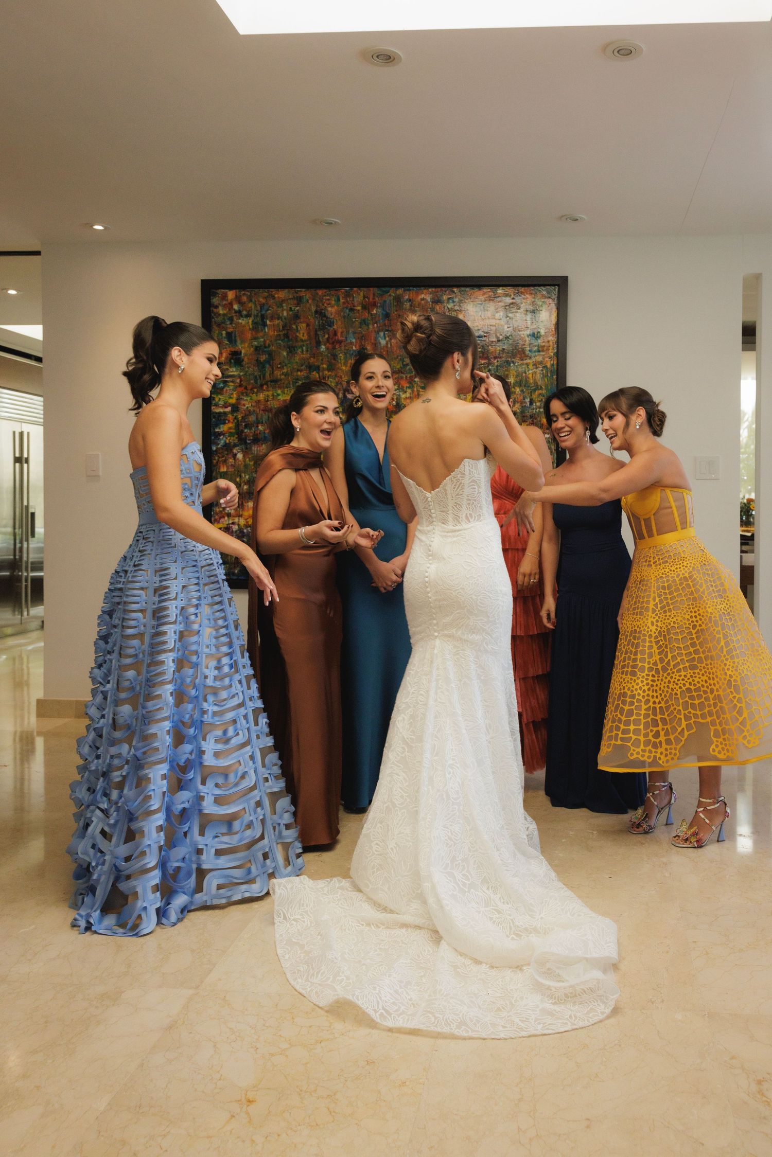 Wedding party gathering in a bright indoor space with bridesmaids in blue and yellow dresses.