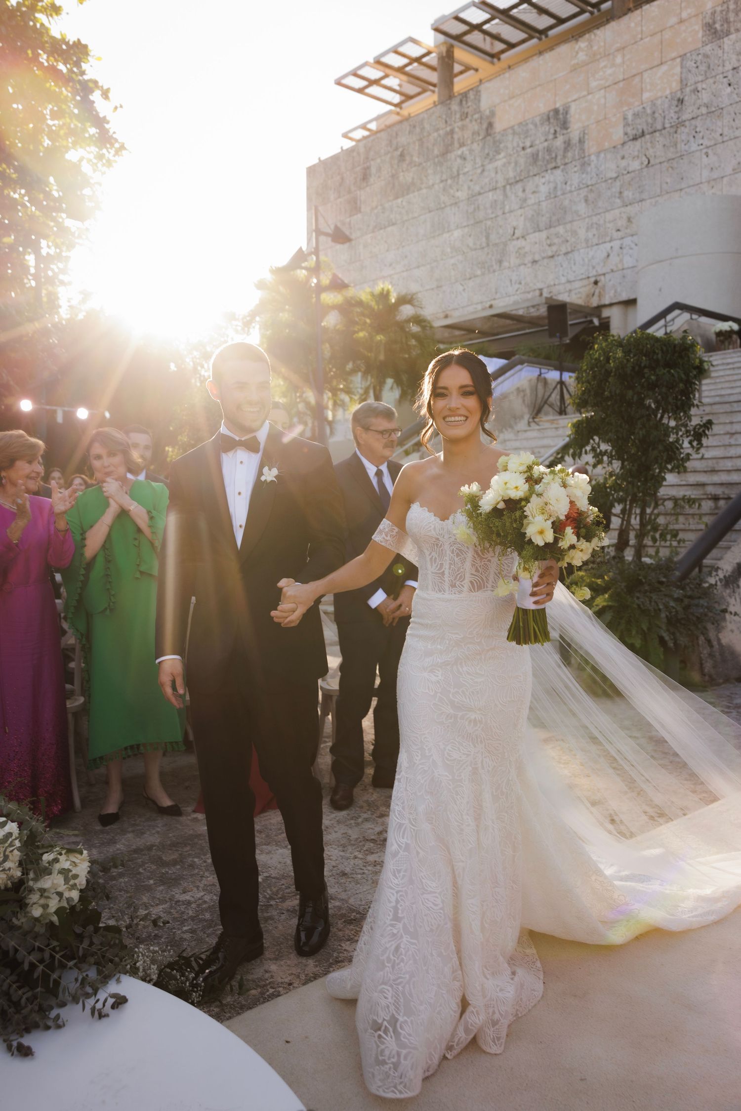 Wedding party poses at sunset against stone wall backdrop with beautiful golden light filtering through.