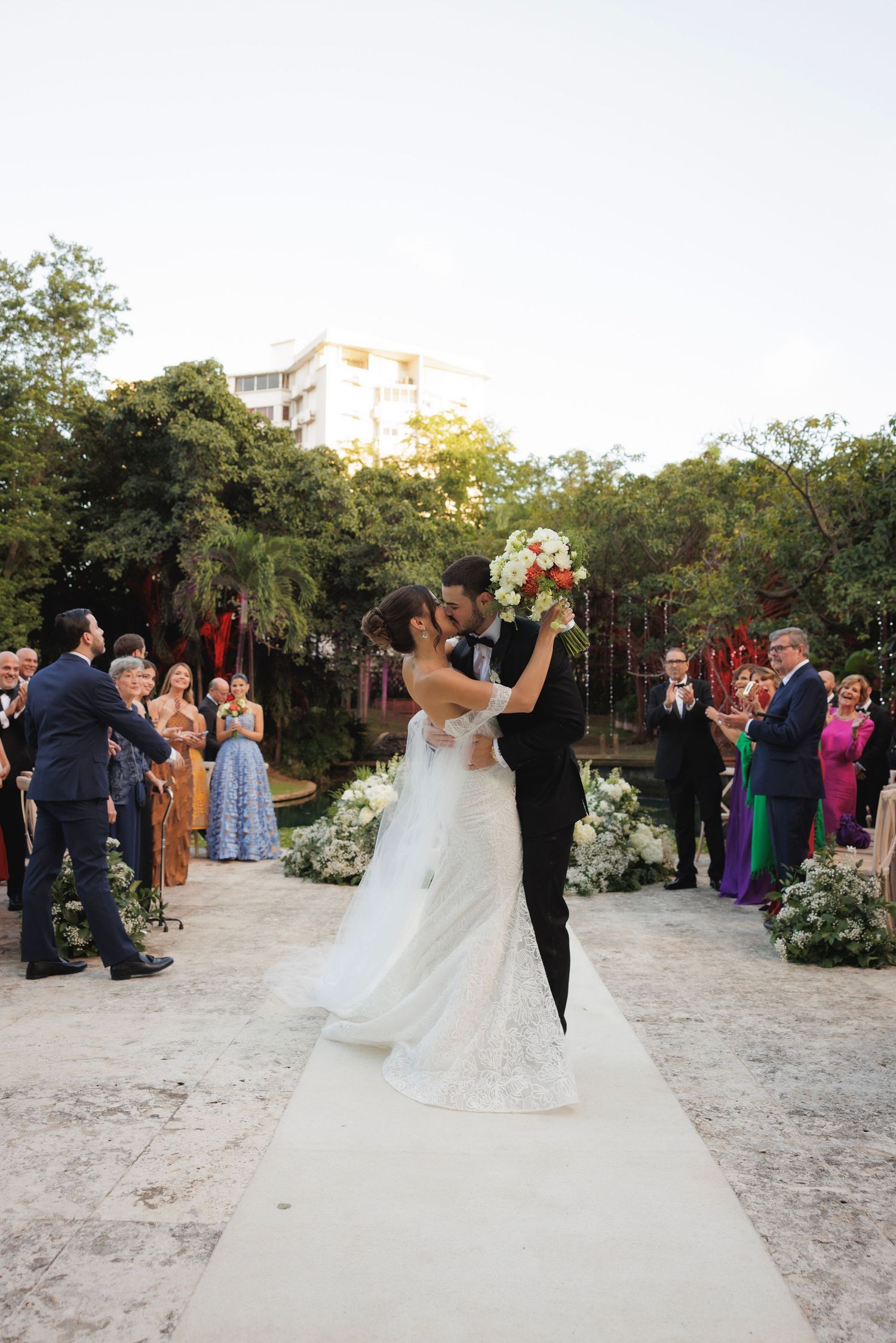 Wedding couple dancing and twirling on a sandy outdoor venue surrounded by guests and trees.
