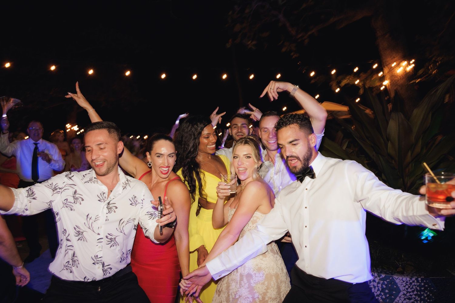 People dancing and celebrating at a lively nighttime party with colorful lighting.