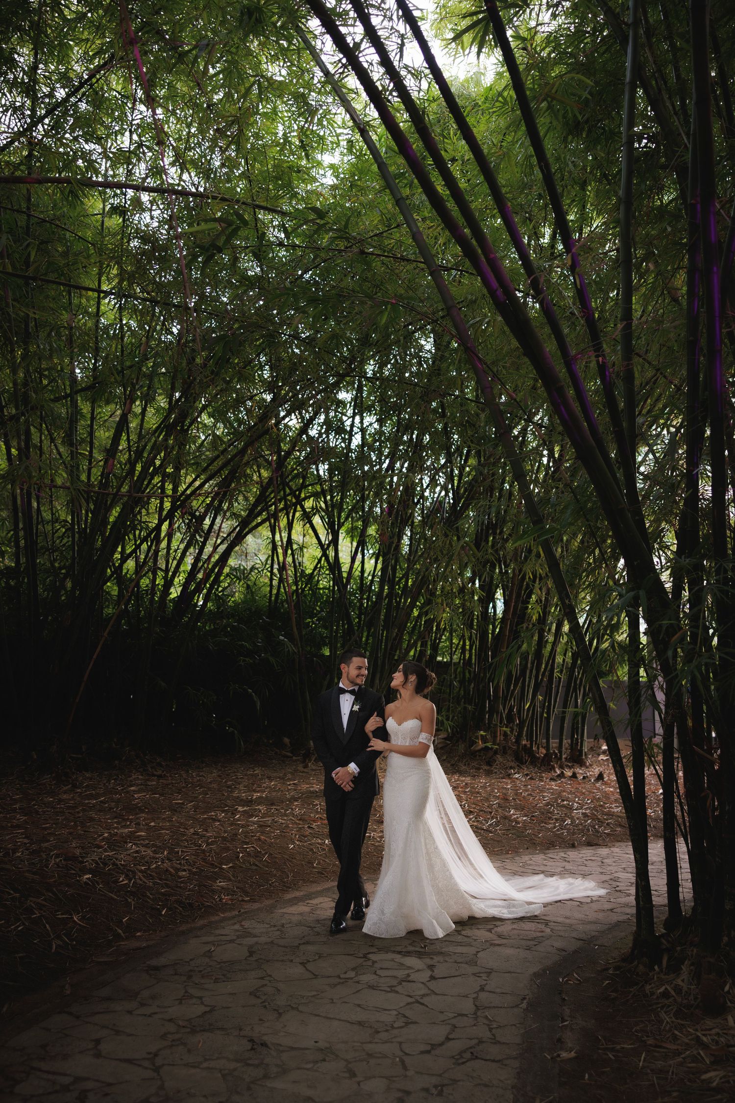 Newlyweds walking together on stone path through bamboo forest garden.