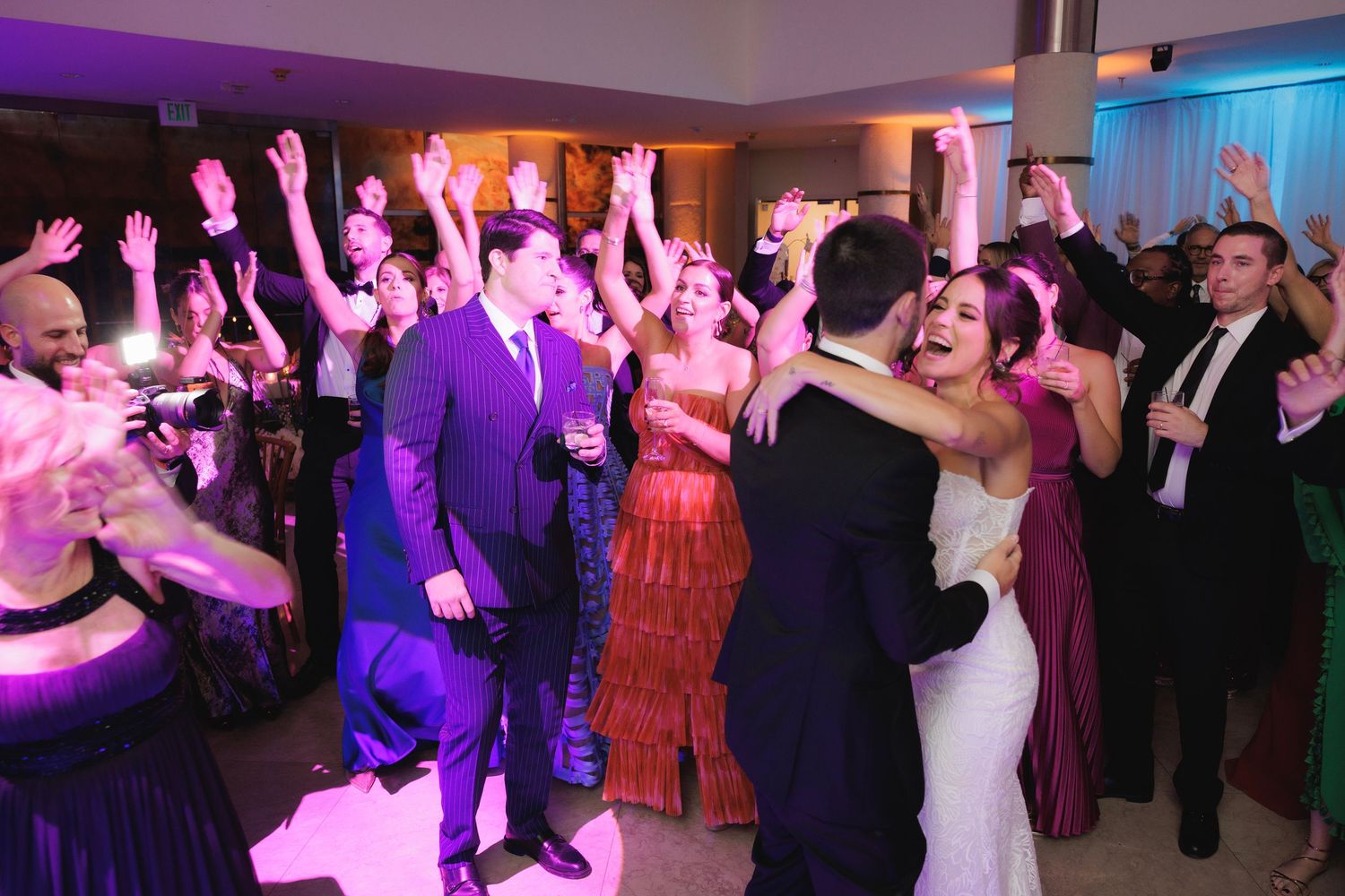 Celebration at an elegant reception venue with guests dancing under vibrant purple and blue lighting.