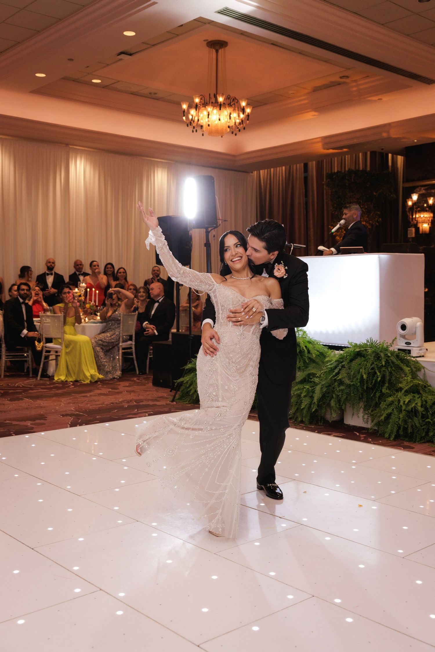 Newlyweds performing their first dance on an illuminated white dance floor at an elegant reception.