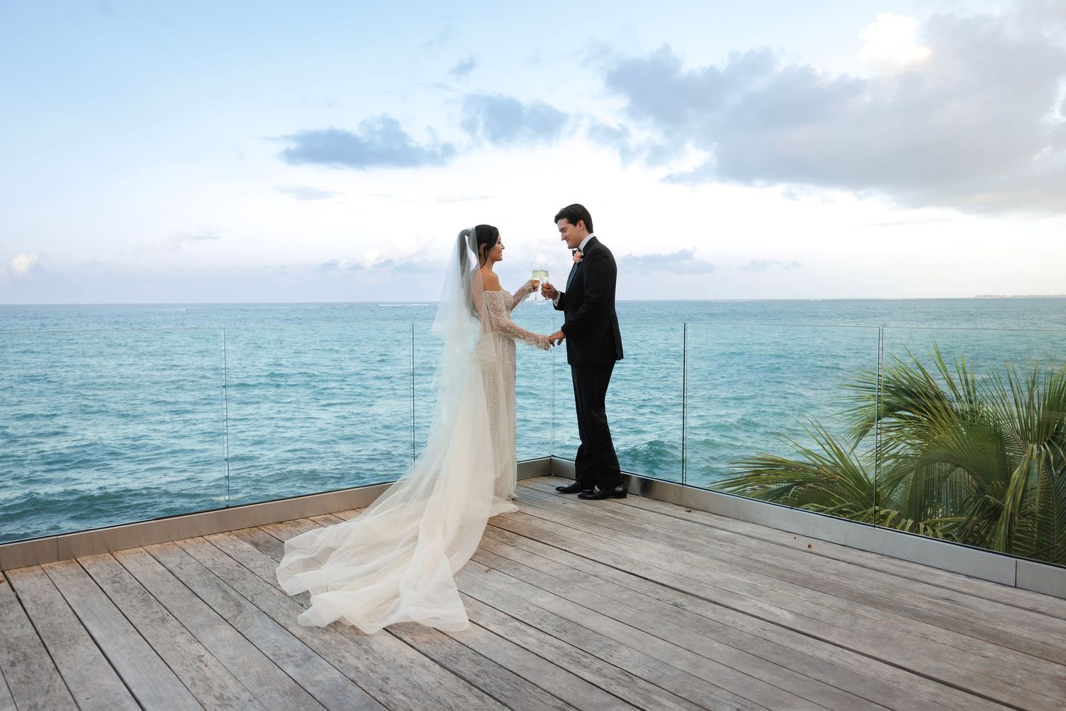 A couple shares a romantic moment on an oceanfront deck during their wedding ceremony at sunset.