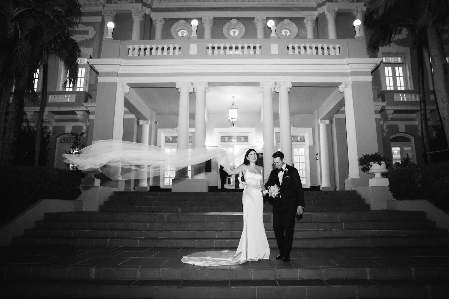 Black and white nighttime portrait of newlyweds on grand architectural steps of historic building.