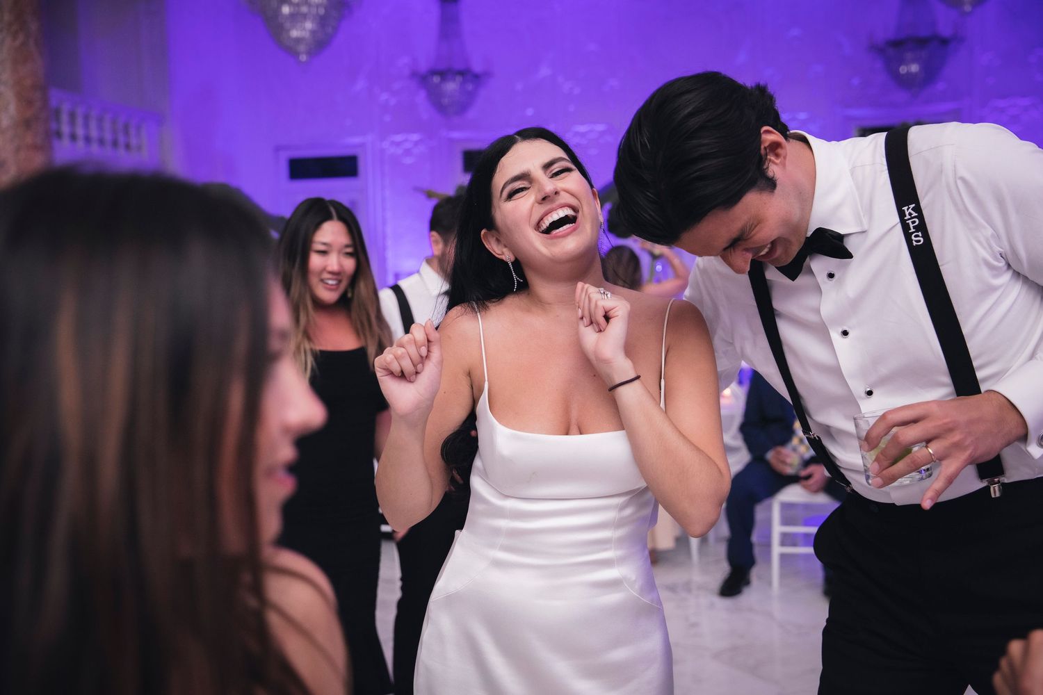 Wedding reception dance party featuring guests enjoying themselves under purple mood lighting in an elegant venue.