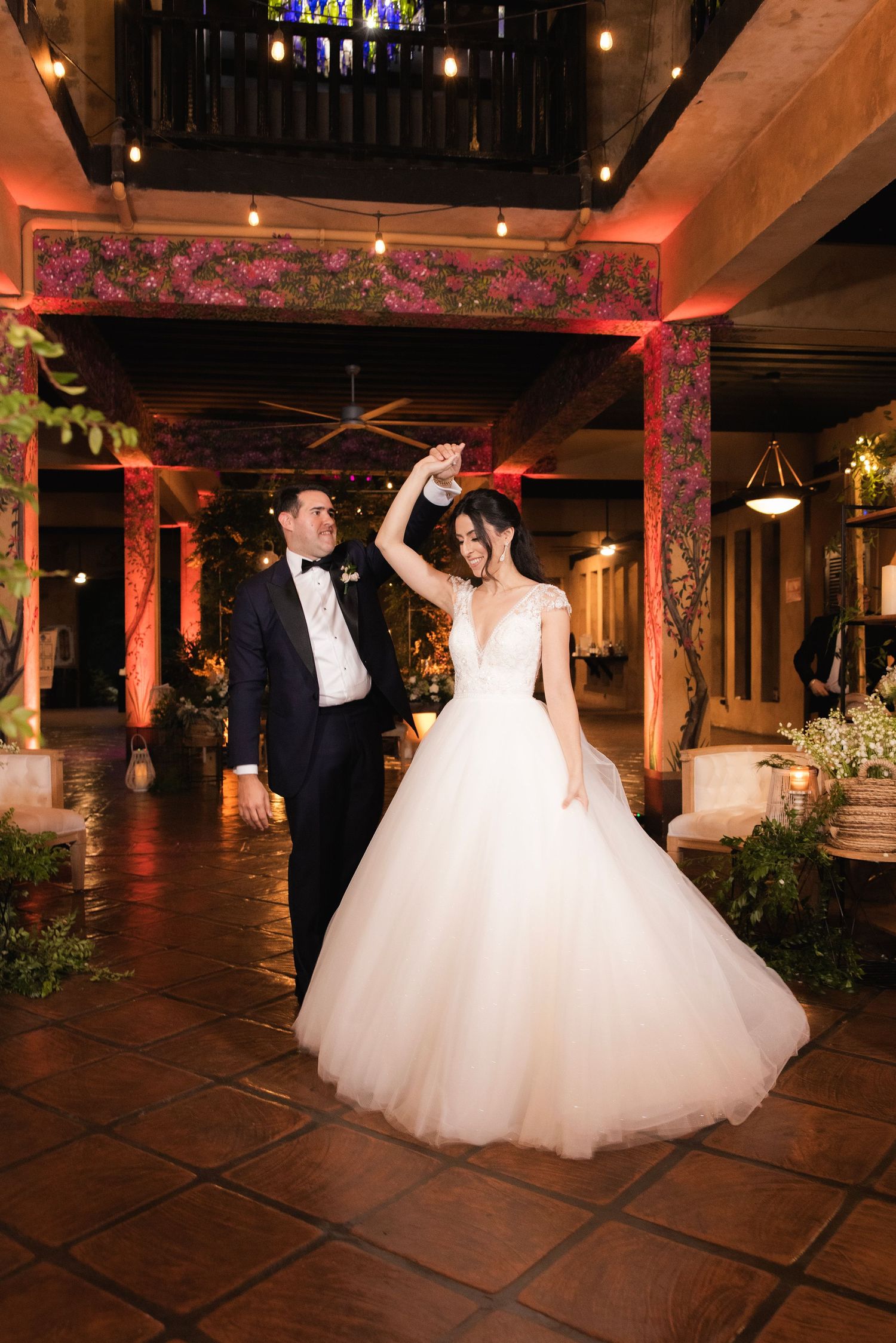 A couple dances under warm lighting in an elegant reception venue with terra cotta floors.