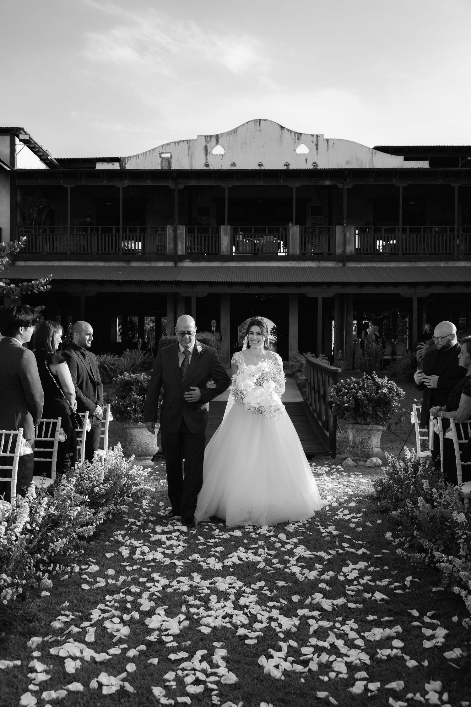 Wedding ceremony setup outdoors with white flower petals scattered along a rustic wooden deck aisle.
