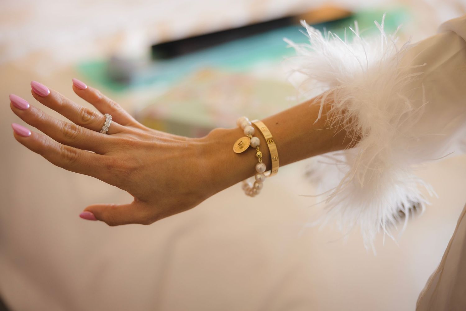 Hand wearing gold bangles and bracelets extends gracefully against a soft white feathery background.