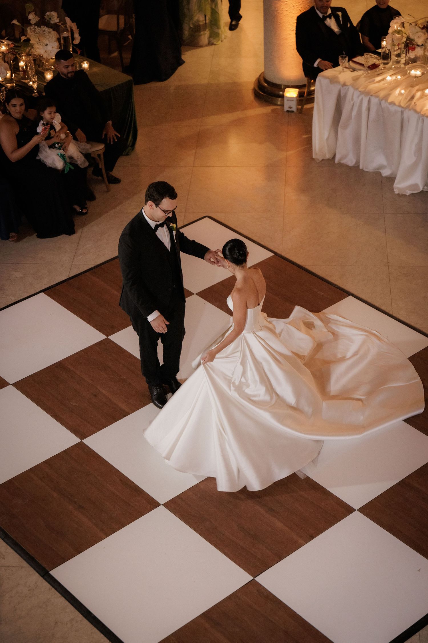 A couple dances elegantly on a black and white checkered dance floor at their wedding reception.
