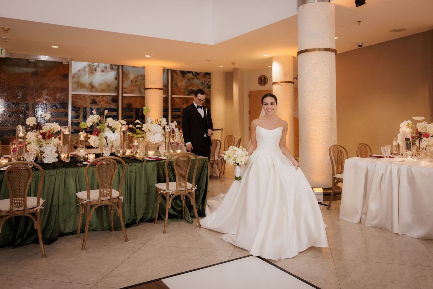 Elegant wedding reception venue with white table settings, chairs, and decorative lighting in a spacious ballroom.
