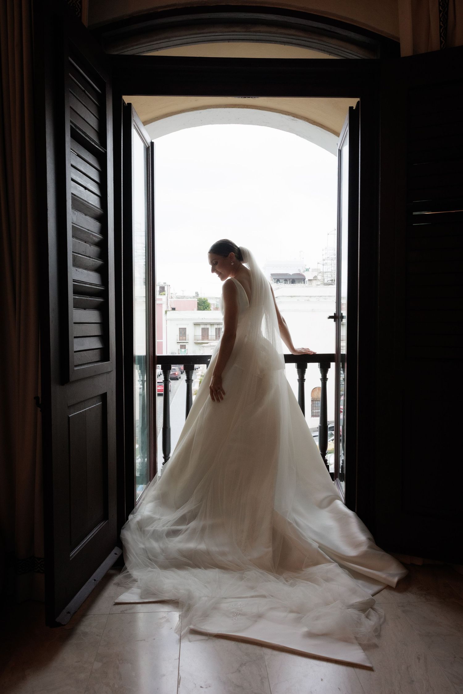 Silhouette of wedding dress against arched window with flowing train.