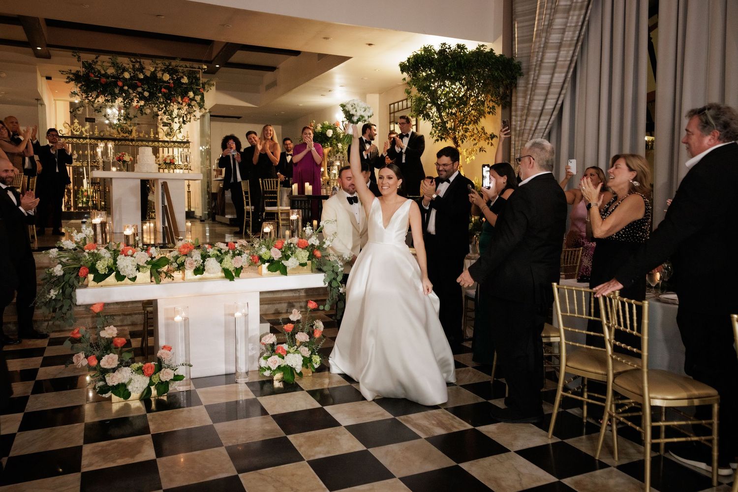 Wedding guests gather around a beautifully decorated reception table with a black and white checkered floor.