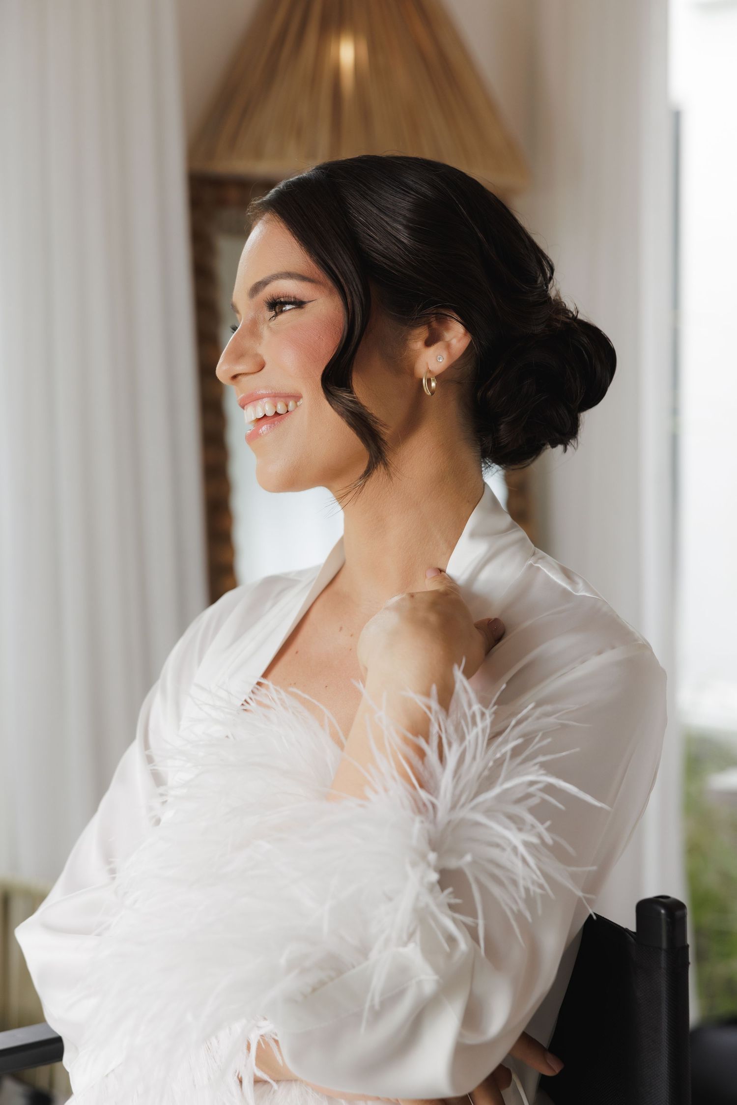 Elegant white feather-trimmed bridal robe photographed in a bright room with soft lighting.