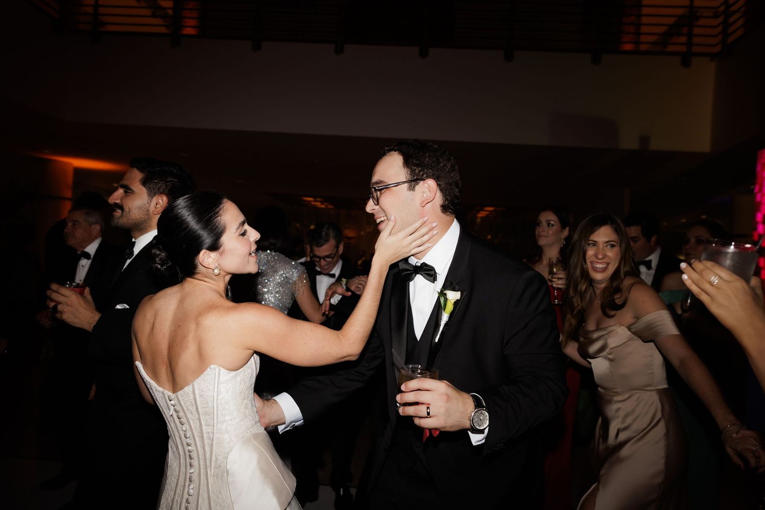 Wedding guests dancing and celebrating on a dimly lit dance floor during an evening reception celebration.