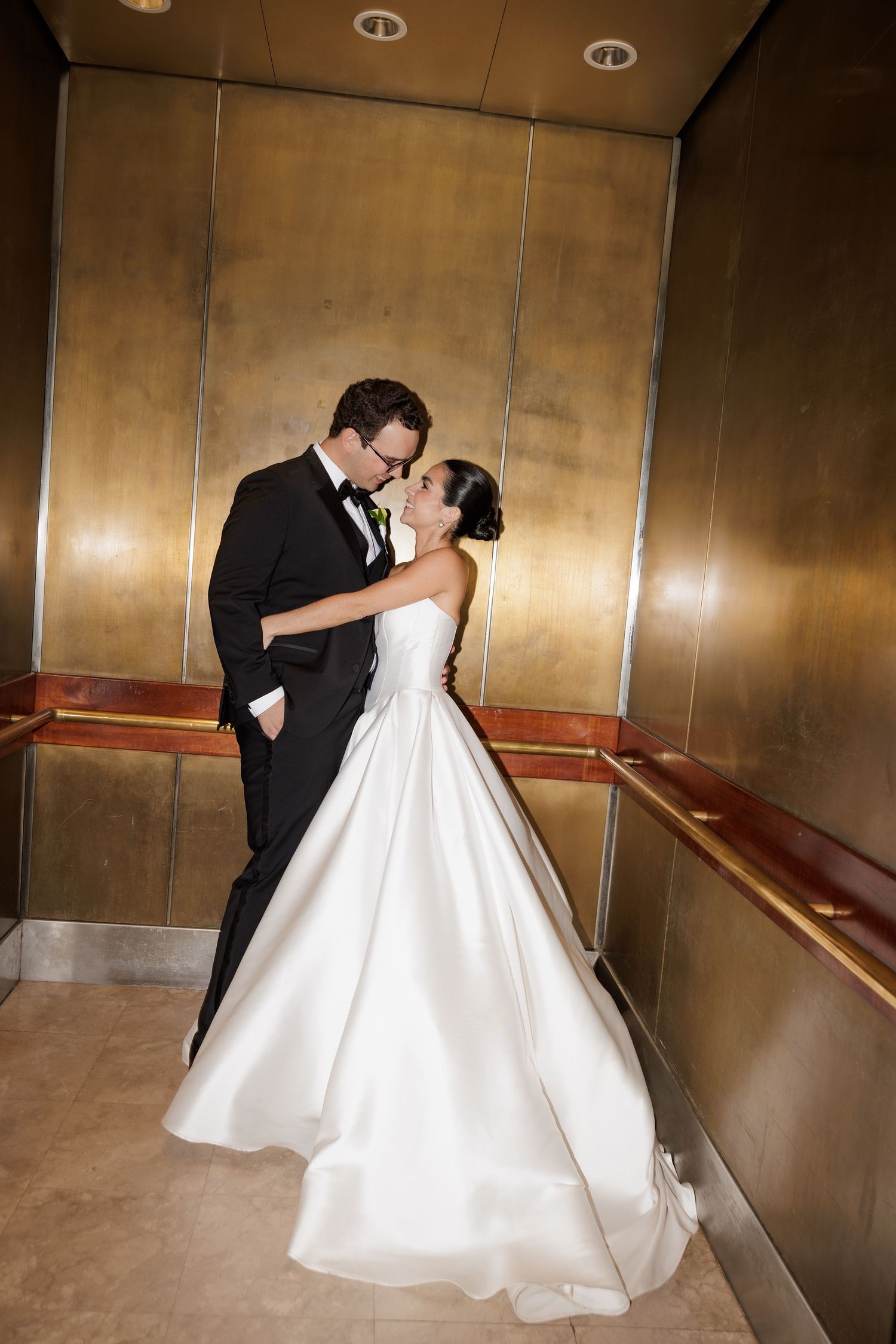 A romantic moment between newlyweds dancing in an elegant venue with golden metallic walls.