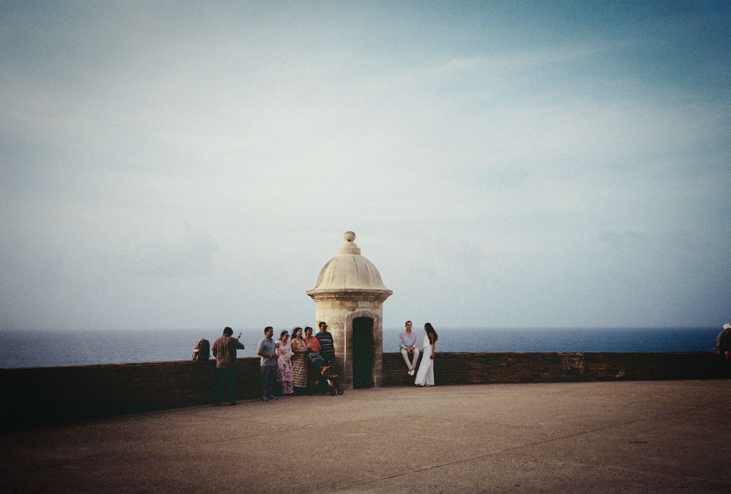 Group of people gathered near a historic stone sentry box overlooking the ocean at El Morro fort in San Juan, Puerto Rico.