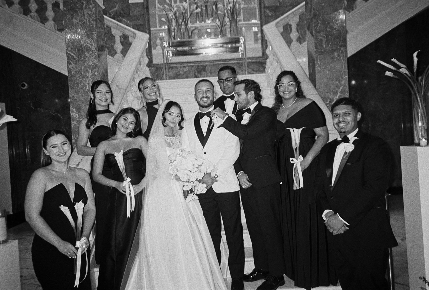 Black and white wedding photo of bride, groom, bridesmaids, and groomsmen posing together in elegant formal attire.
