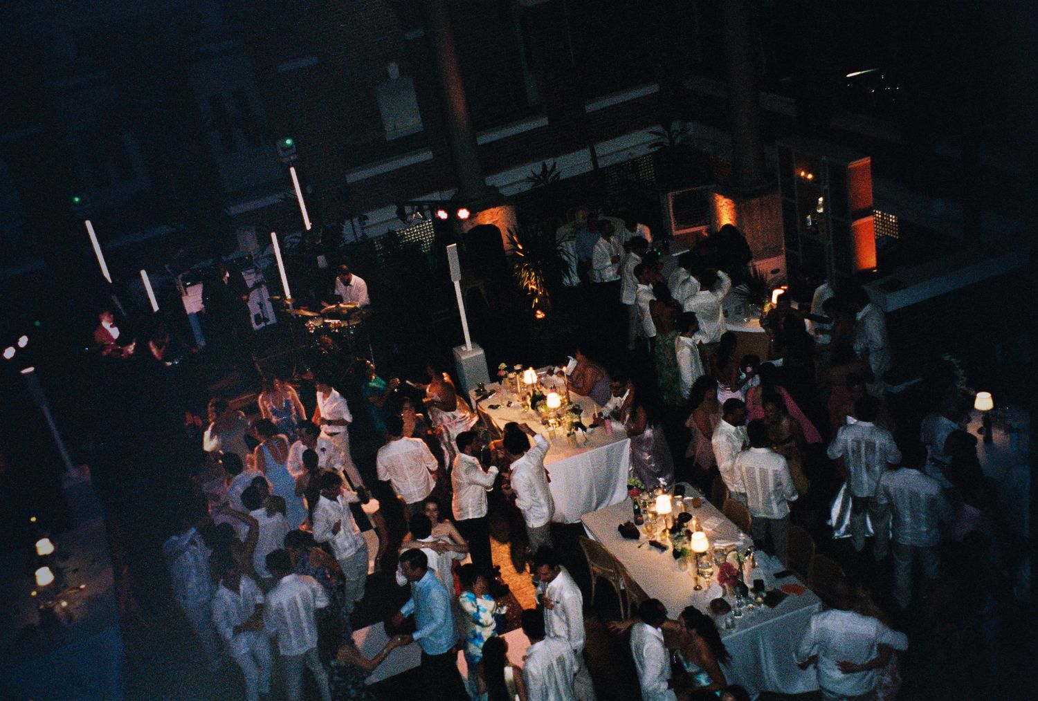 Aerial view of elegant wedding reception with guests in white attire gathered around candlelit tables.