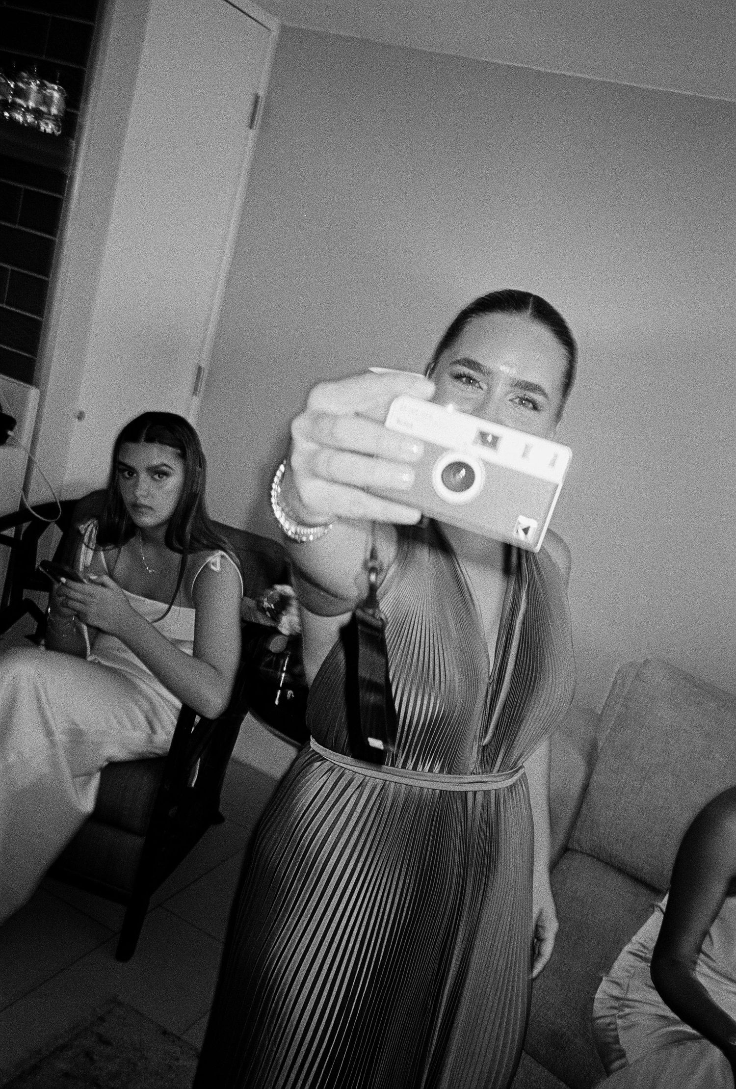 Woman taking selfie with instant camera in black and white photo at indoor gathering with friends.