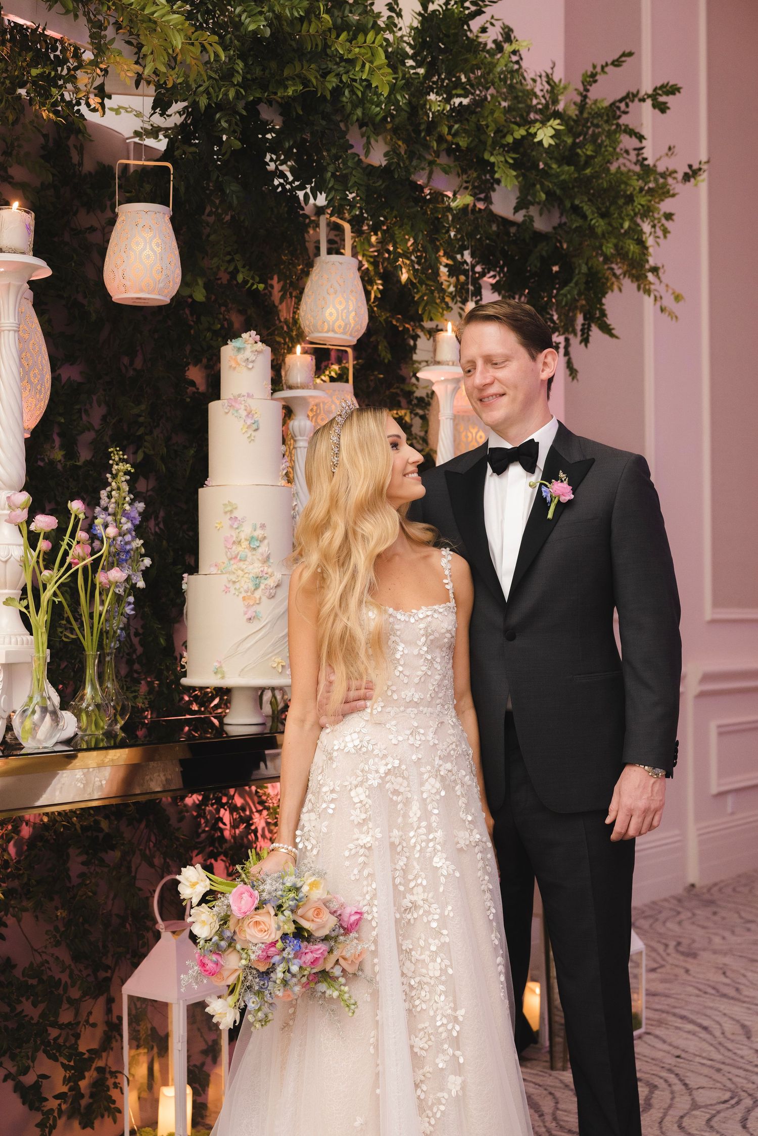 An elegant wedding scene with rustic lanterns, a tall white cake, and lush greenery decorations.