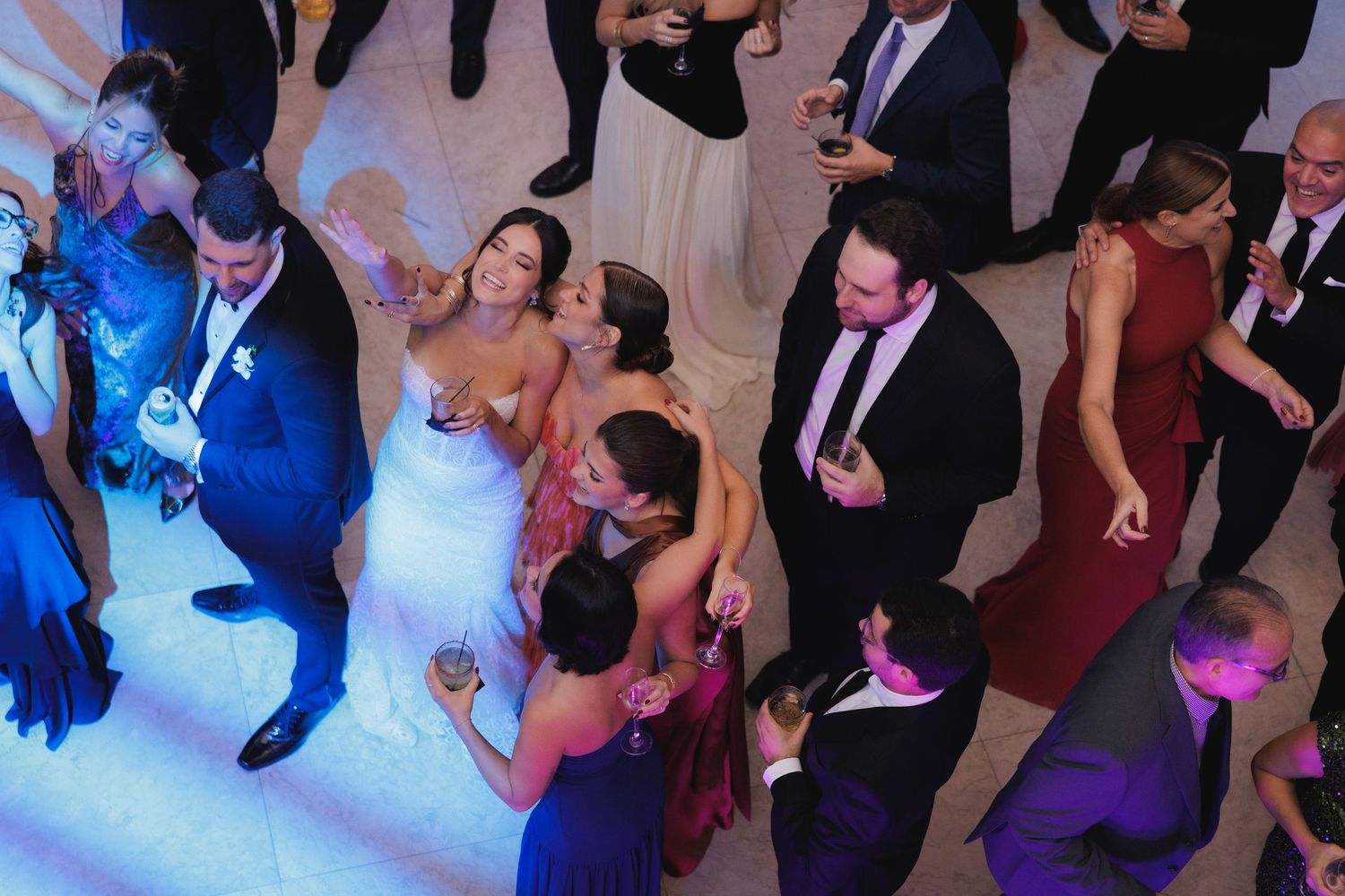 Wedding guests dancing at a reception with colorful dance floor lighting and formal attire.