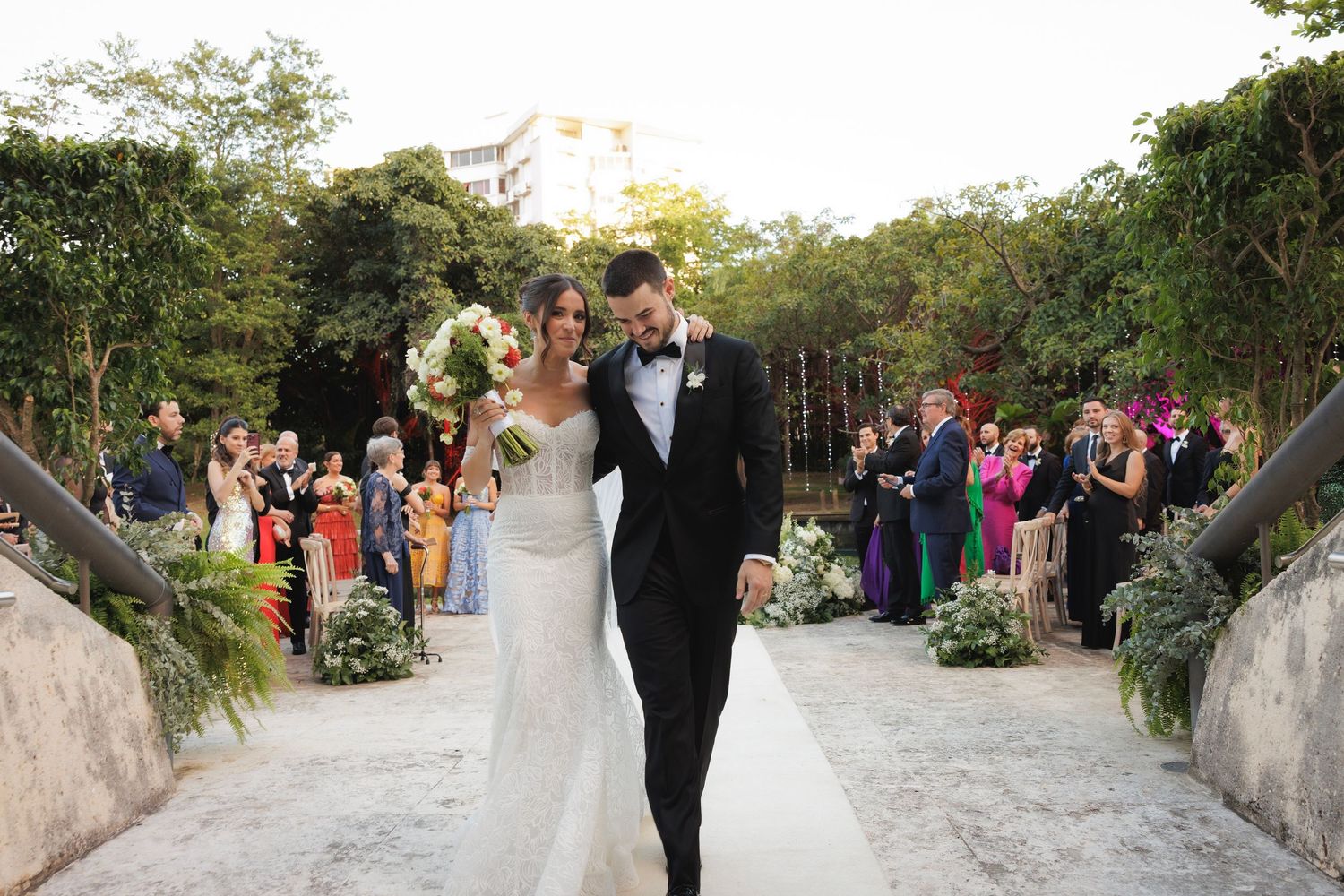 Stone pathway lined with guests at outdoor wedding celebration surrounded by natural greenery.