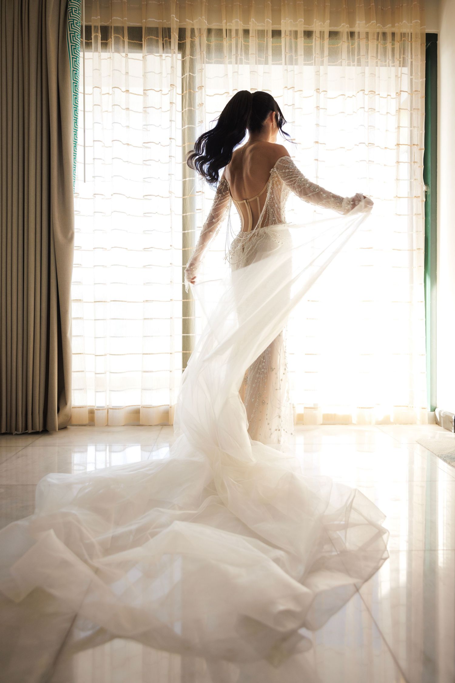 Wedding dress swirling in dramatic motion near bright window with sheer curtains.