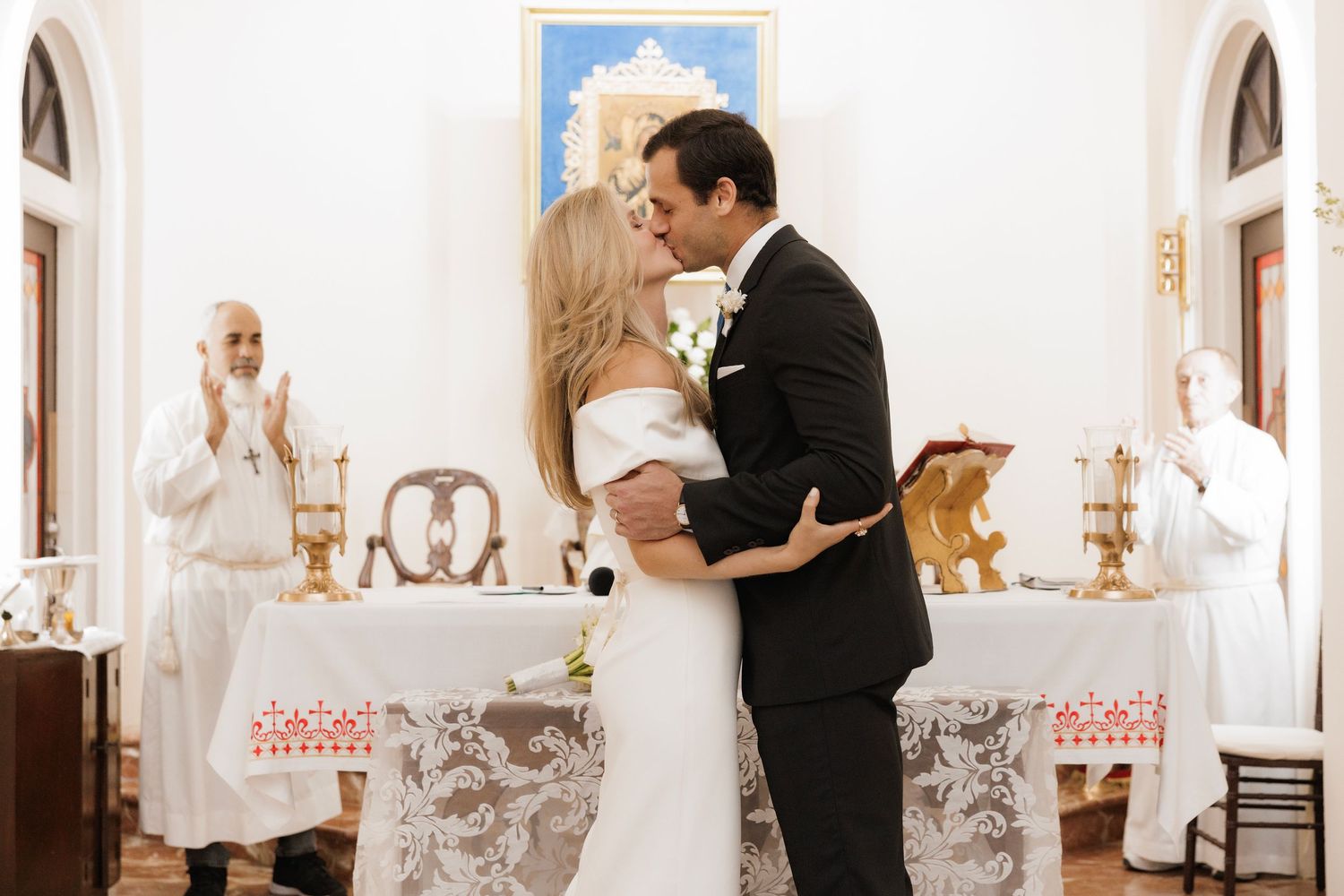 A couple shares an intimate moment during their first dance as newlyweds in an ornate white reception venue.