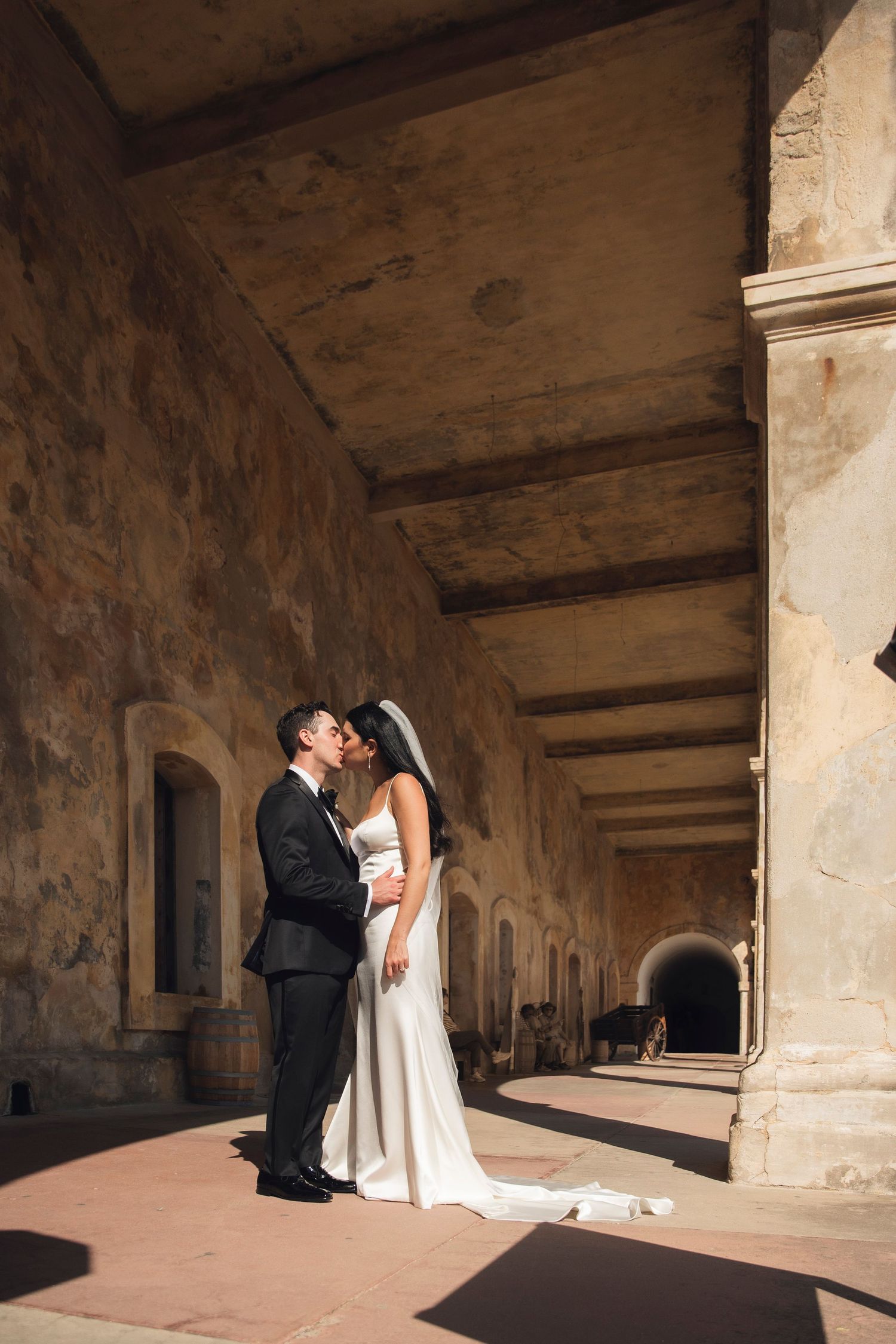A wedding couple shares a romantic moment under stone archways at a historic venue.
