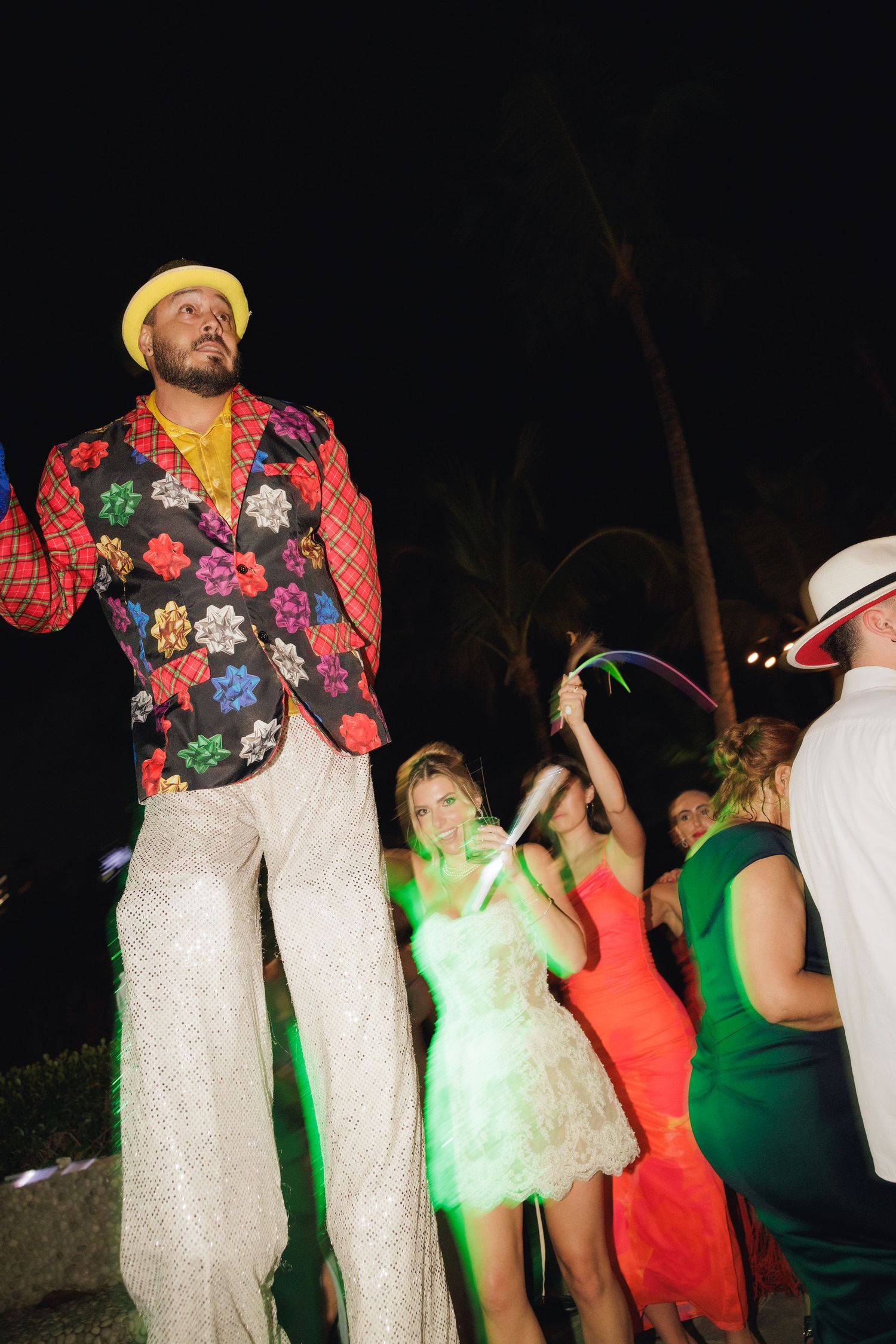 A group in colorful dresses and outfits dances in a line at an outdoor nighttime event.