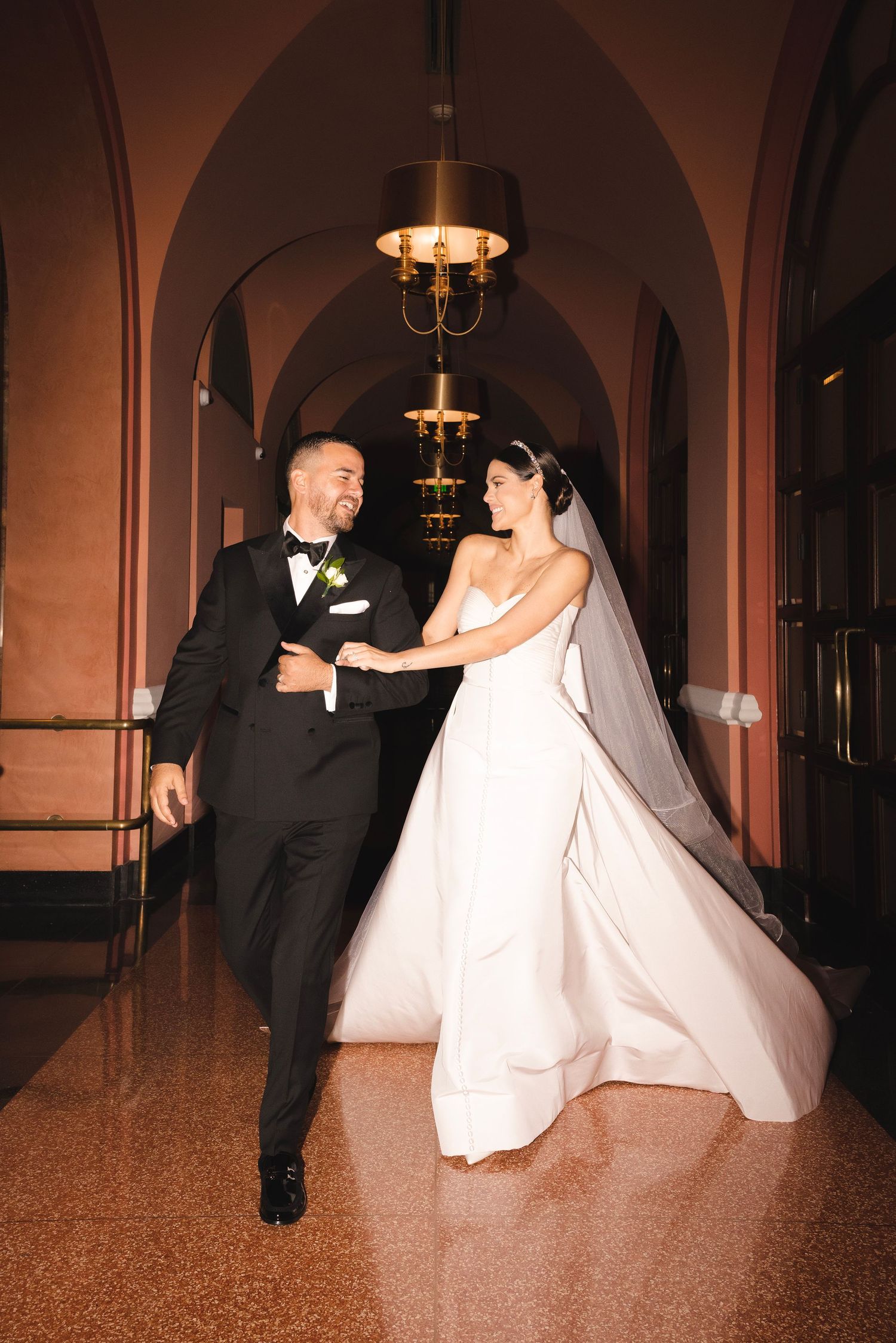 Dancing newlyweds in formal attire perform dips and twirls in an elegant hallway with arched ceilings and warm lighting.