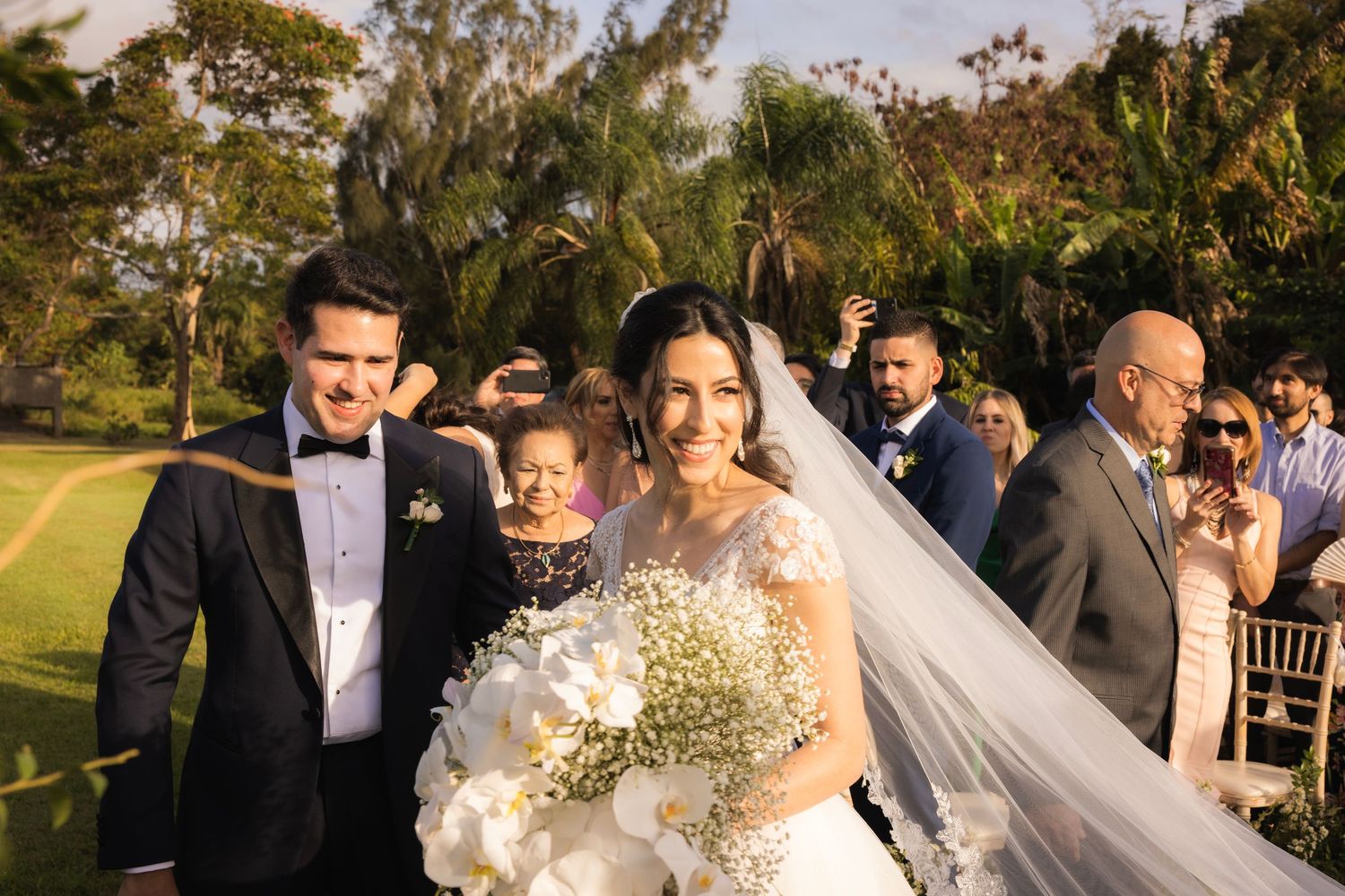 Outdoor wedding ceremony guests gathered on lawn chairs with floral decorations.