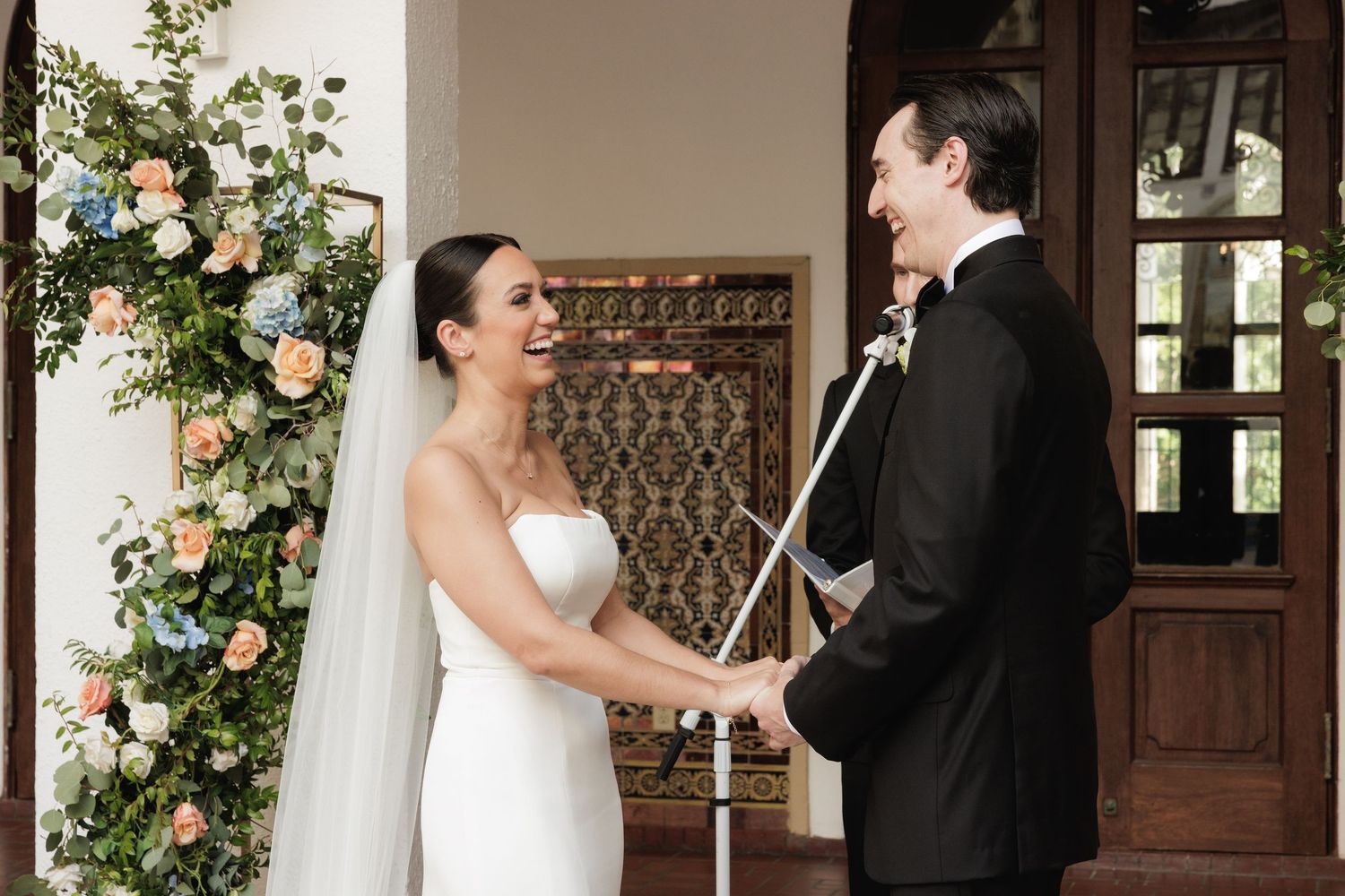 Bride and groom share an intimate moment in front of a rustic wooden door adorned with floral decorations.
