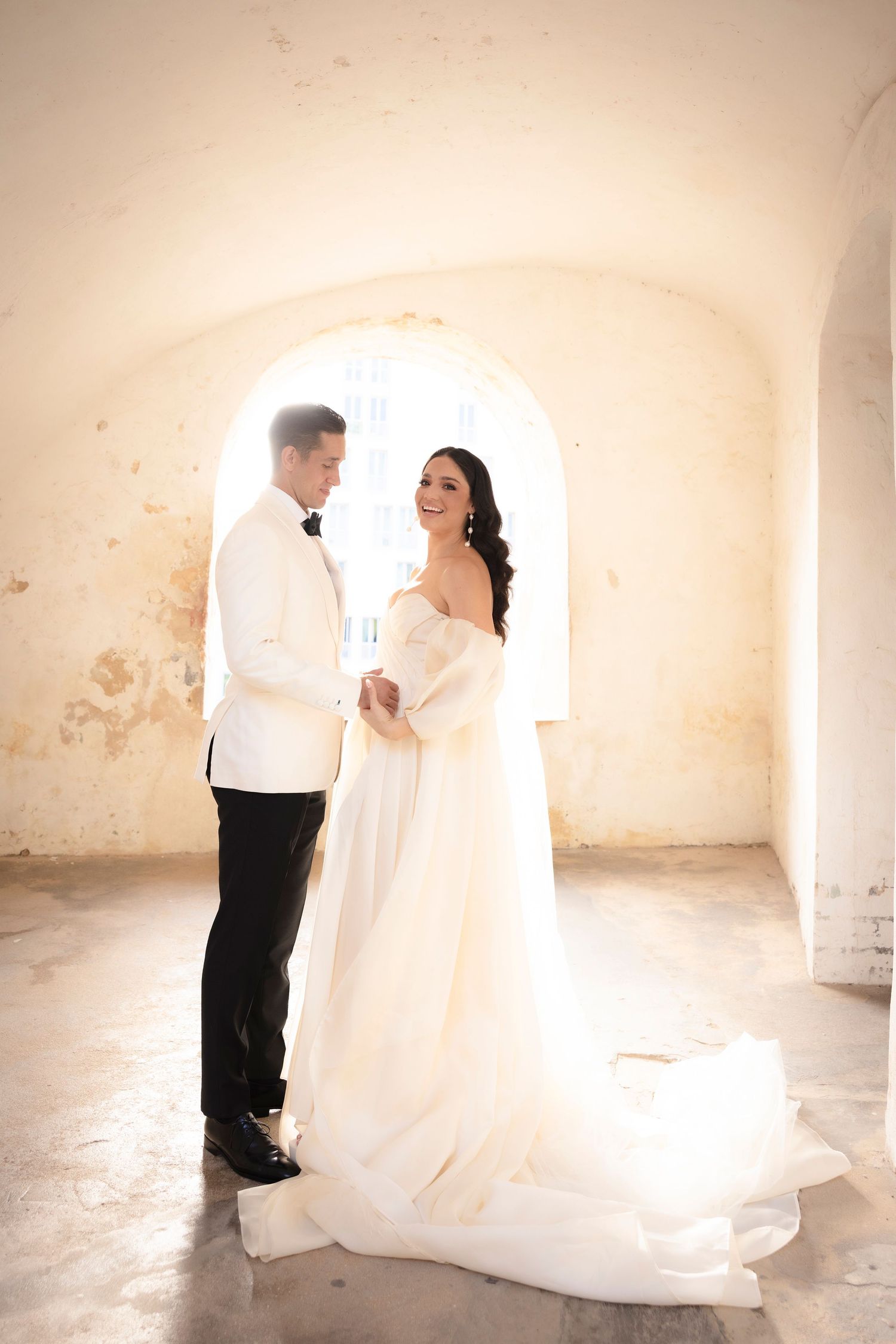 Wedding couple in white attire sharing intimate moments in a rustic stone room.