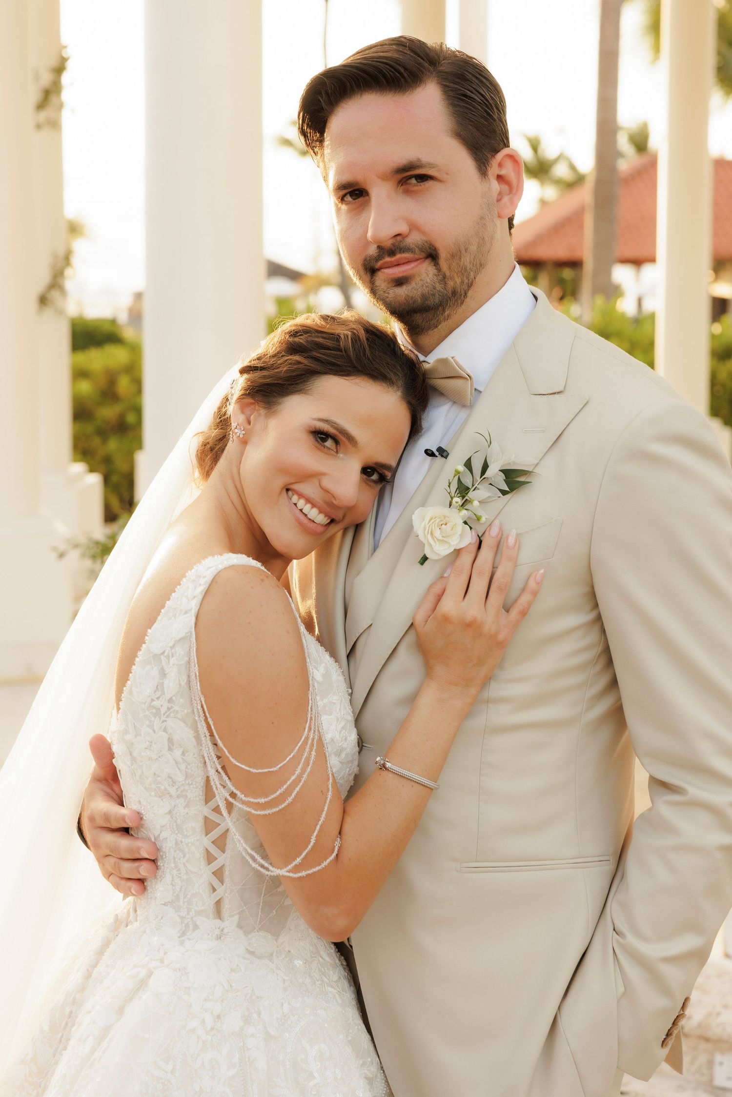 Happy newlyweds embrace and pose together among white columns in elegant wedding attire on their special day.