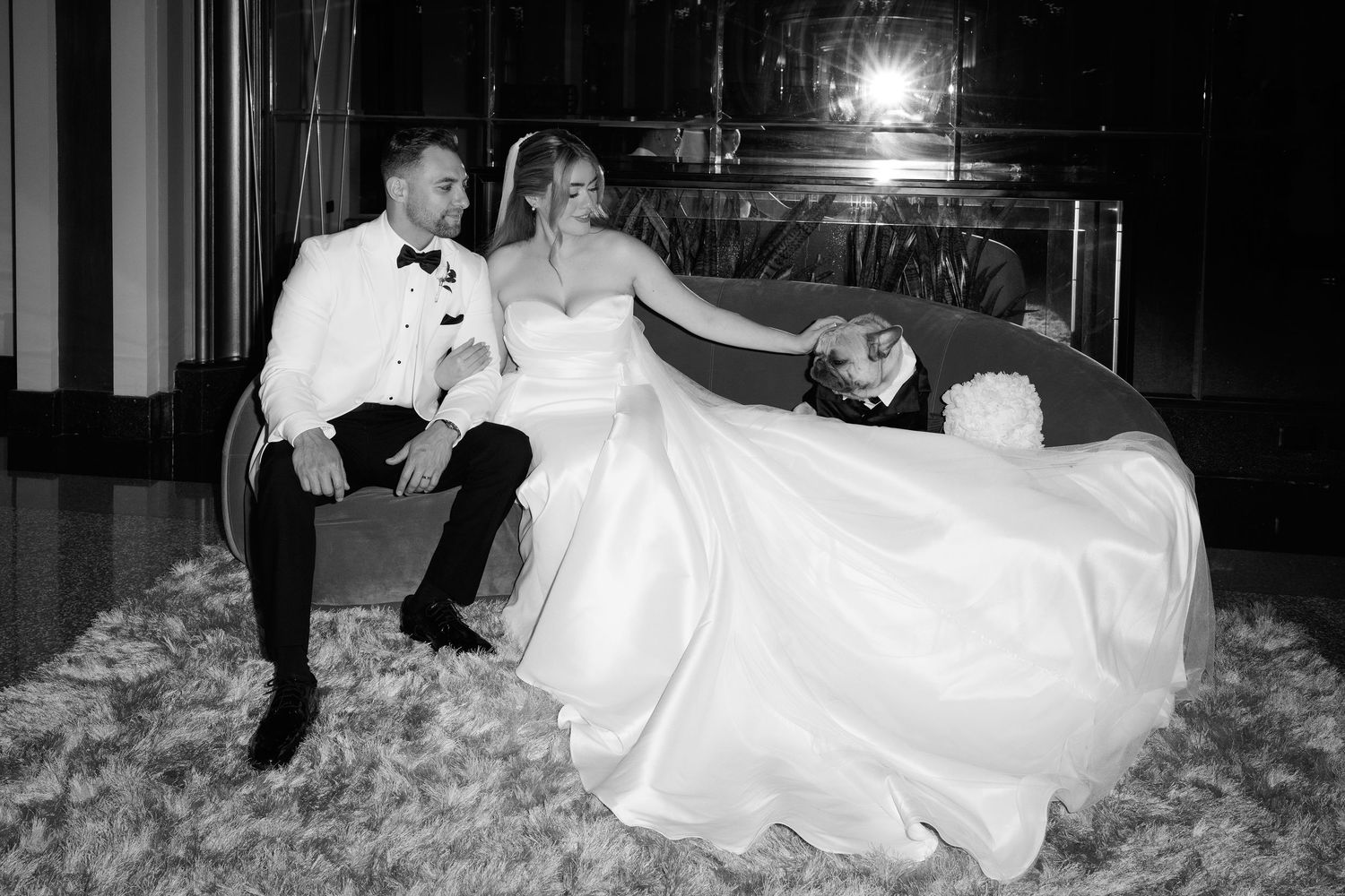 A black and white wedding photo showing a couple relaxing on the floor at their reception venue.