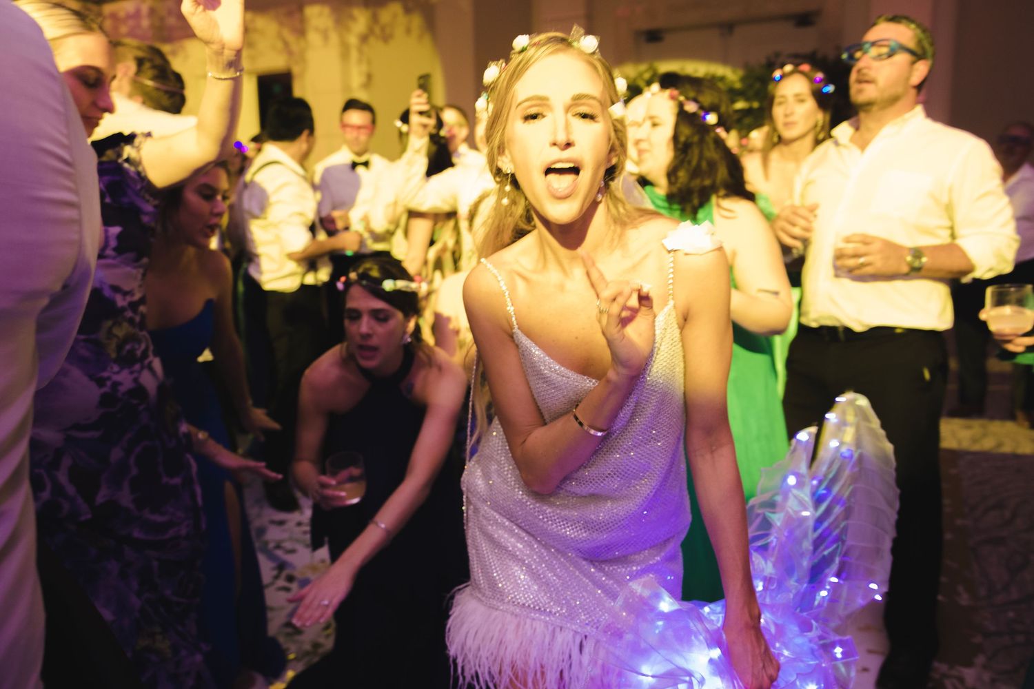 A lively dance party in progress with people dancing and celebrating under colorful purple lighting.
